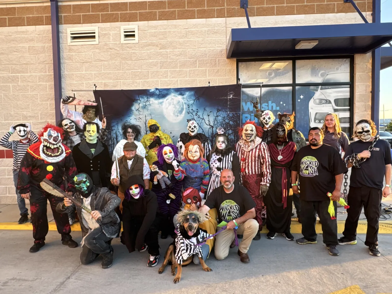 Group of people and a dog in spooky Halloween costumes posing outside a building with a full moon backdrop.