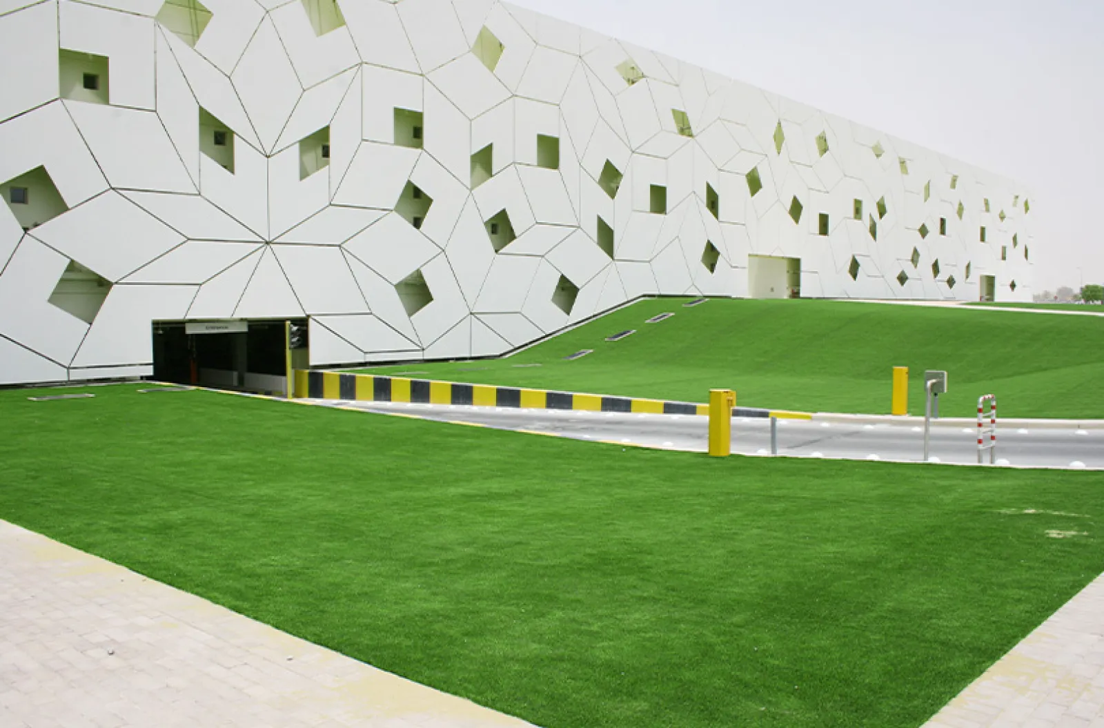 Modern building with geometric white facade and green landscaped lawn with road and barriers in the foreground