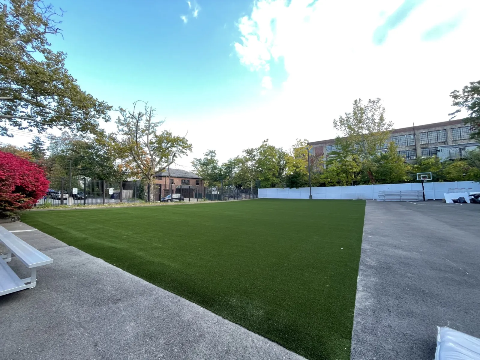 a green lawn with a fence and trees and buildings in the background