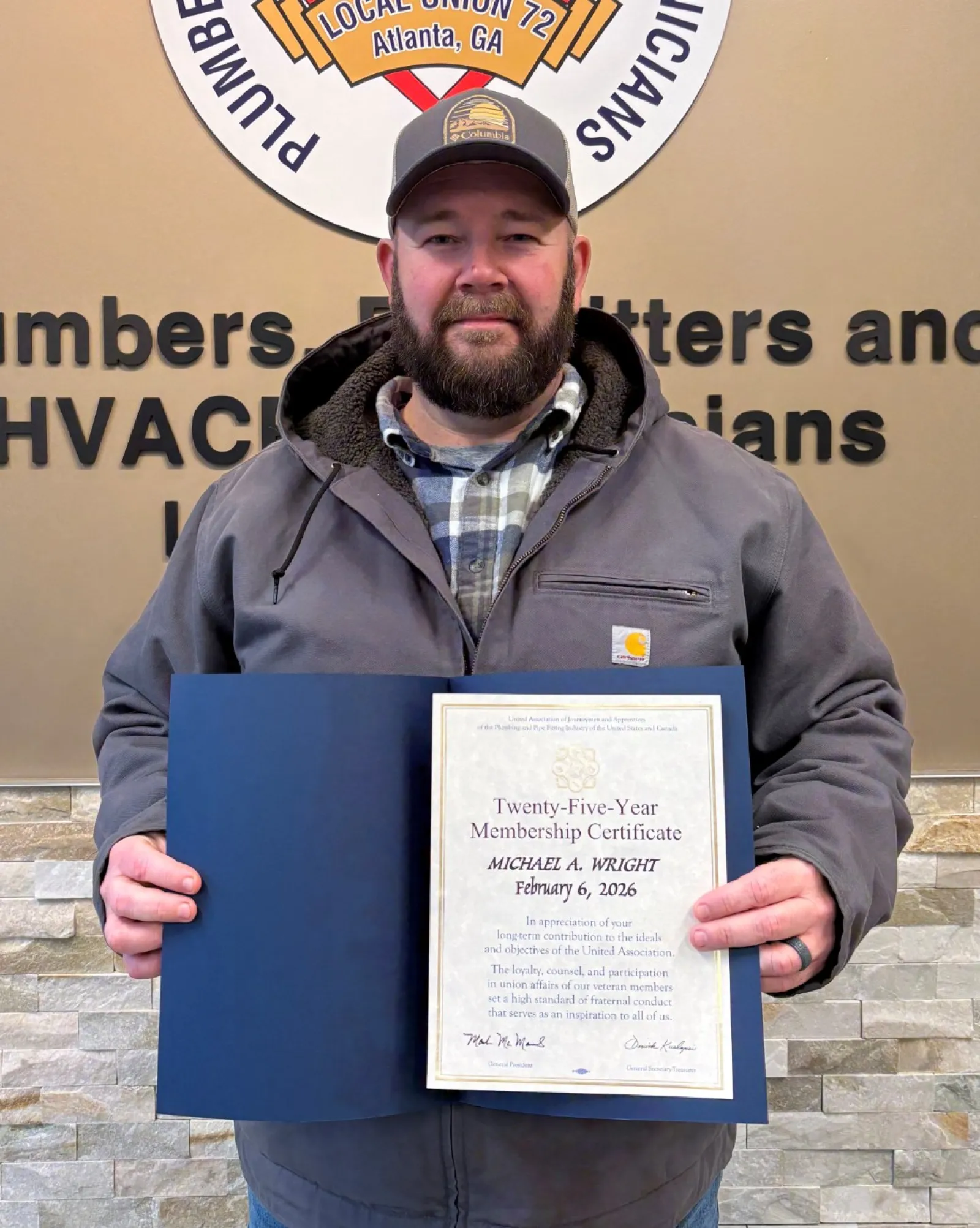 Man holding certificate in front of Plumbers, Pipefitters and Service Technicians union sign on wall