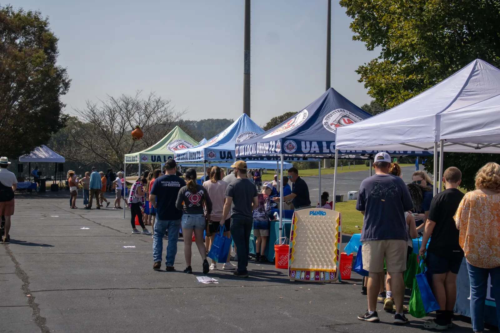 Outdoor community event with people gathered under branded tents playing games like Plinko on a sunny day.