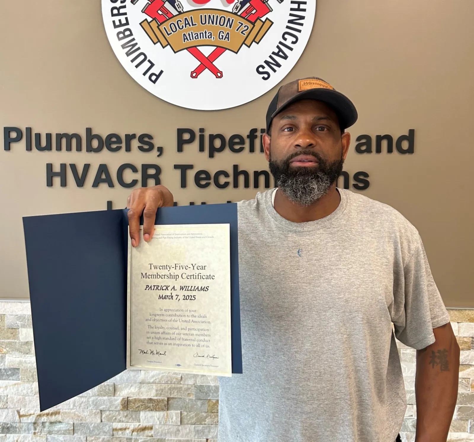 Man holding a certificate standing next to Plumbers and Pipefitters union sign on wall