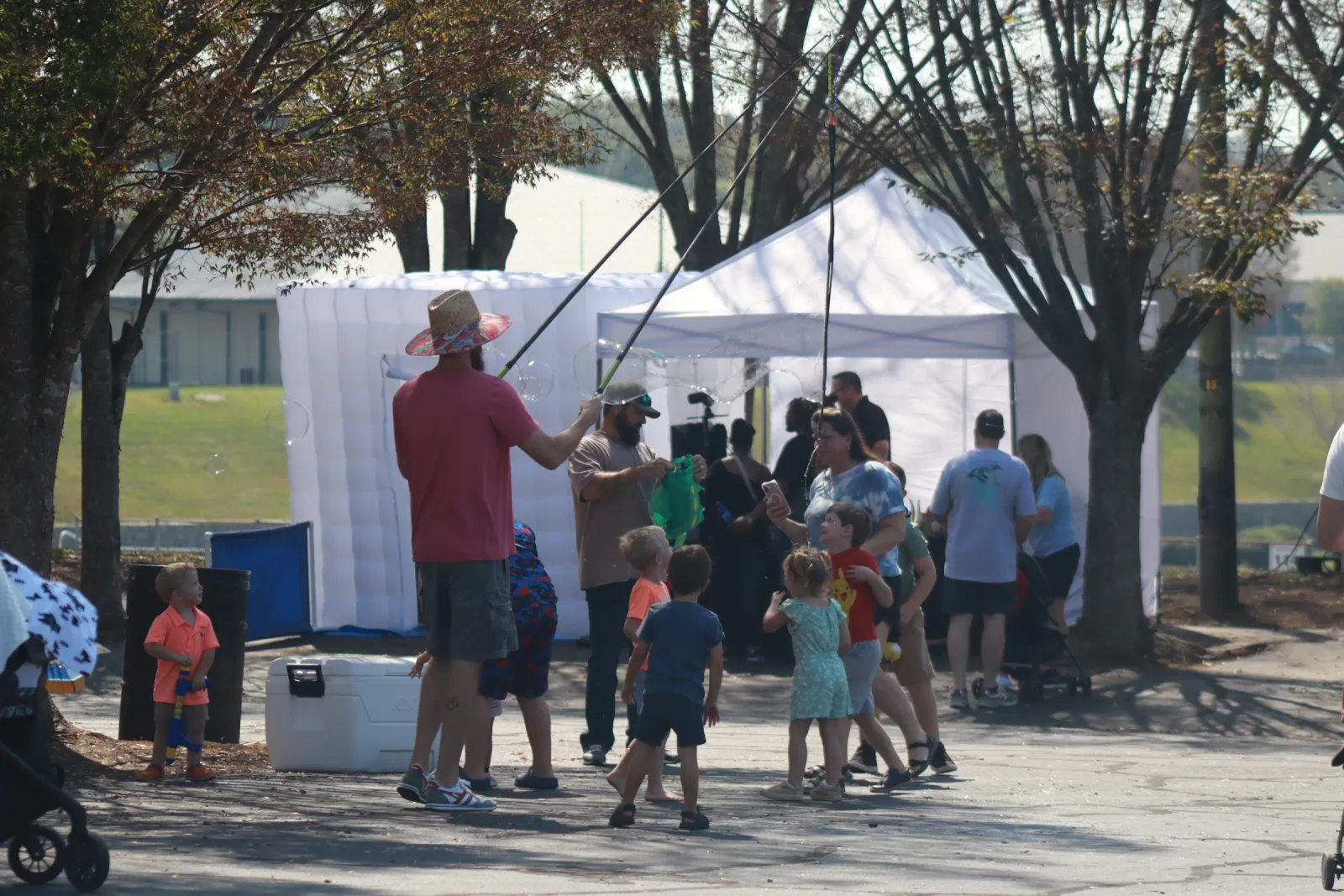 Adults and children gathered outdoors near tents, engaging in a fishing activity on a sunny day with trees around.