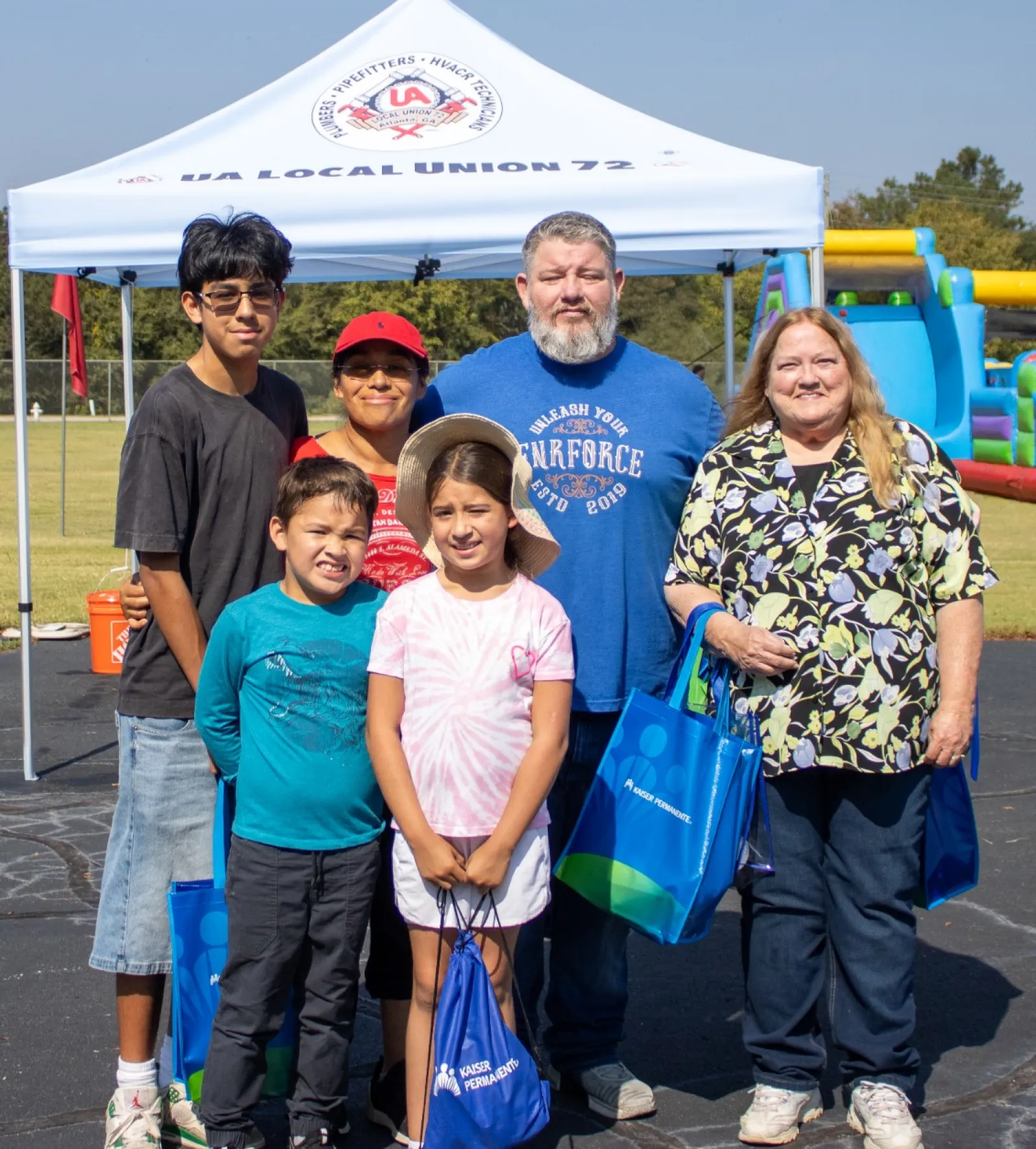 Group of six people posing at an outdoor event with a union tent and inflatable play structure in background.