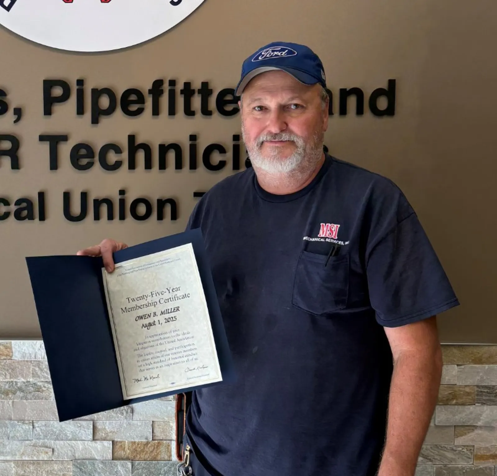 Man standing next to Plumbers and Pipefitters union sign holding a certificate inside a building.
