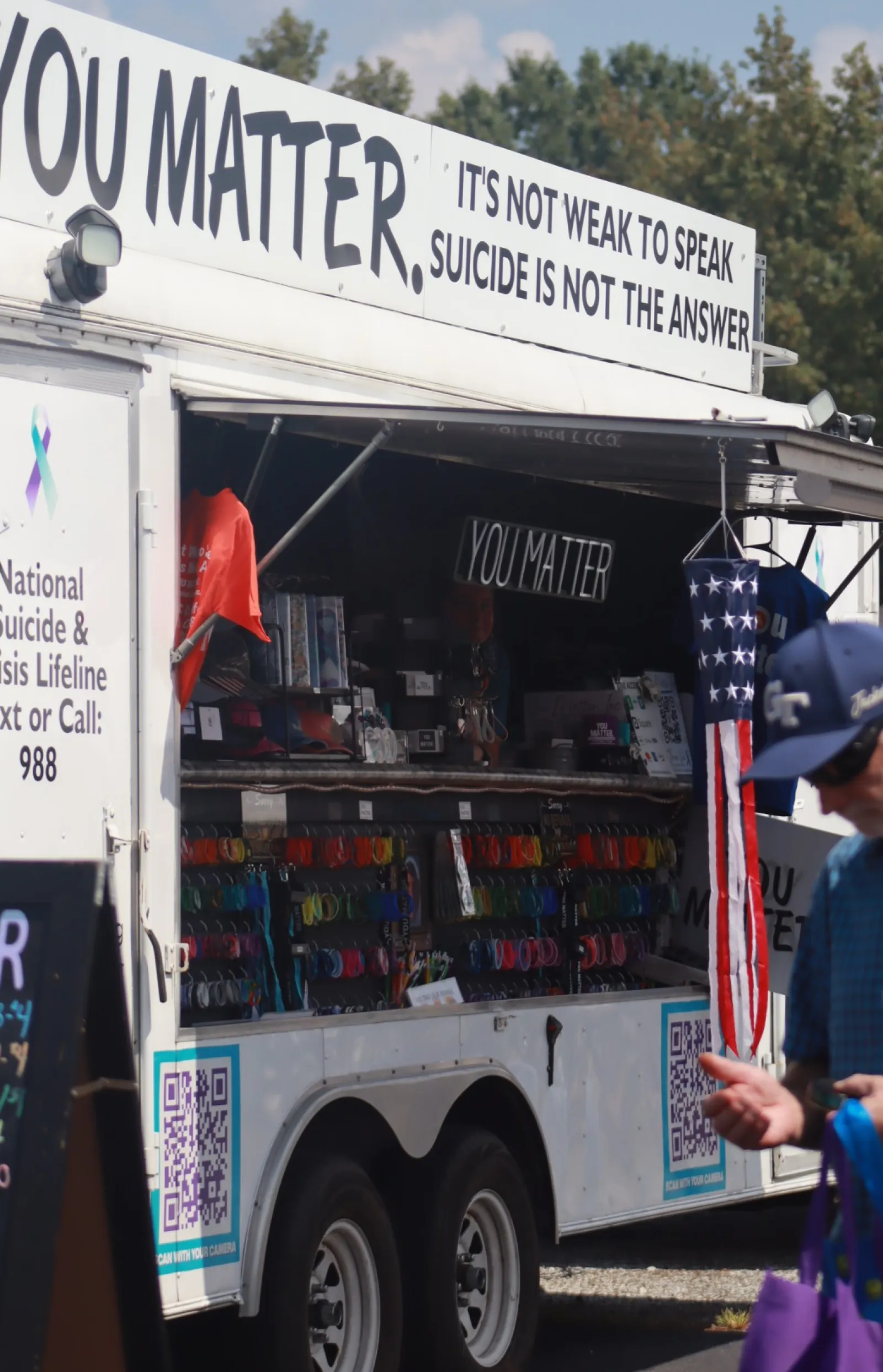 Mobile suicide prevention booth with YouMatter and hotline info, a man walking nearby under blue sky