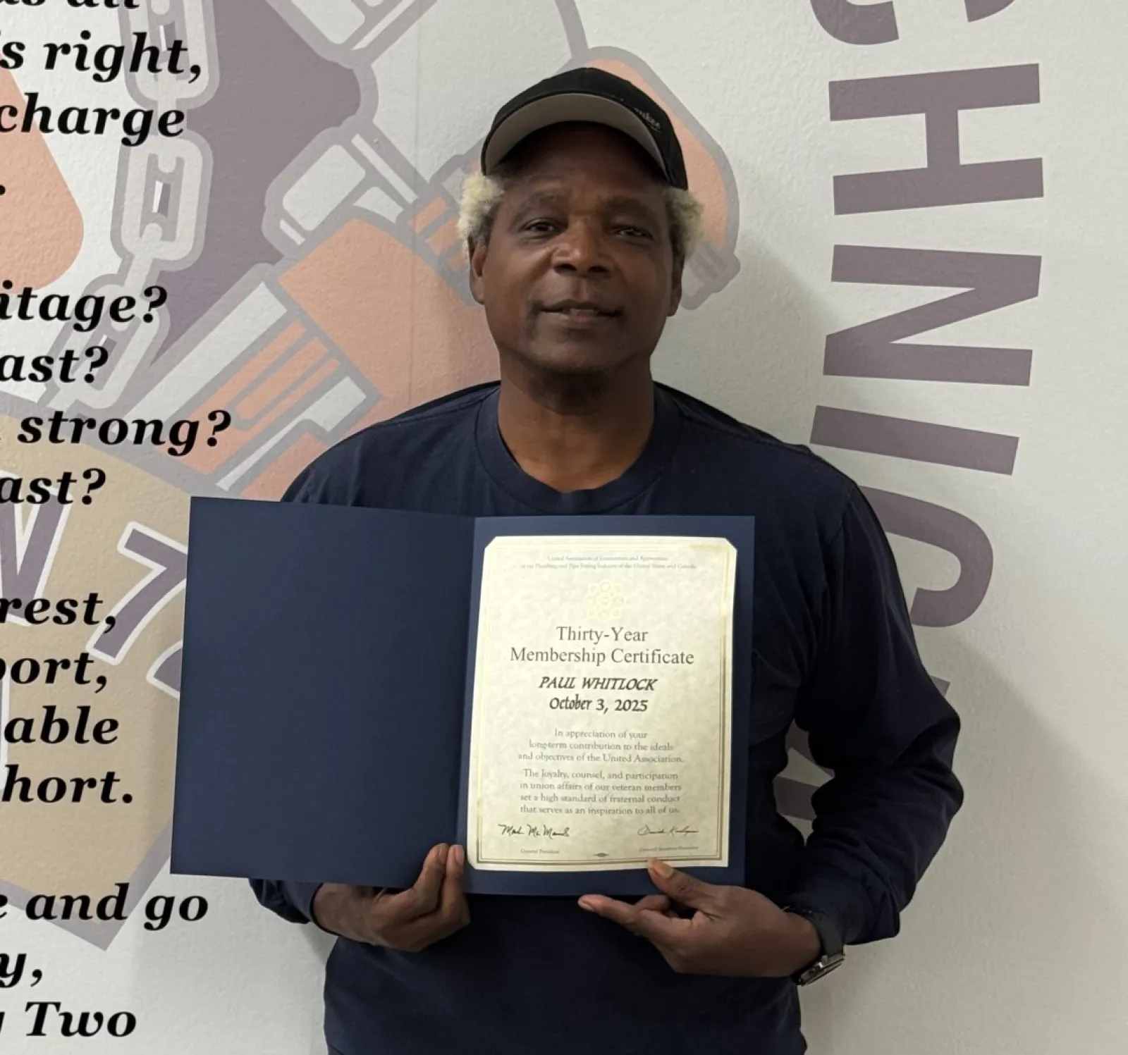 Man holding a thirty-year union membership certificate standing in front of a wall with union-related text and logo.