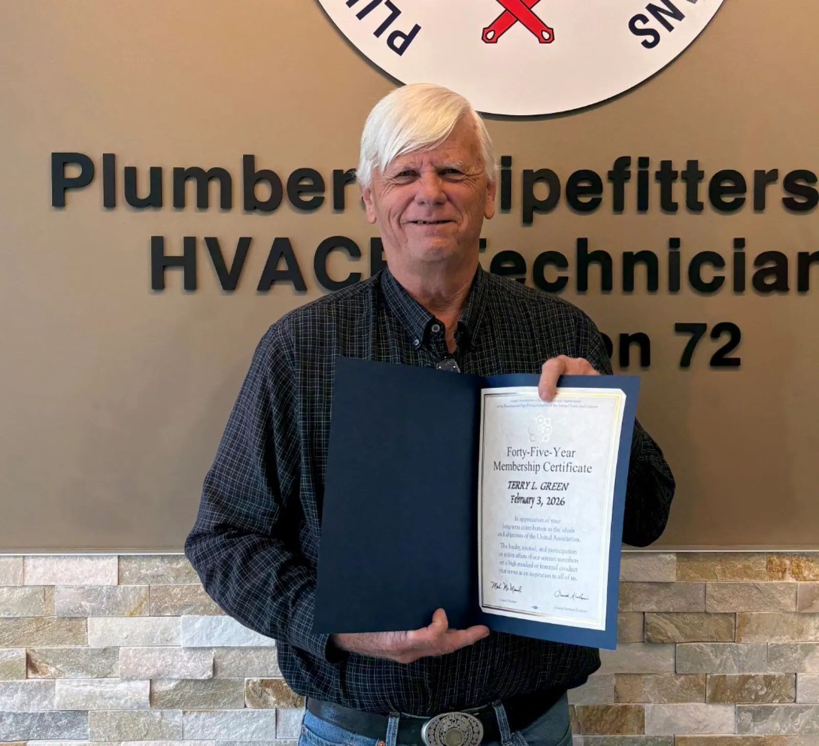 Man holding certificate standing in front of Plumbers and Pipefitters Local Union 72 sign in office