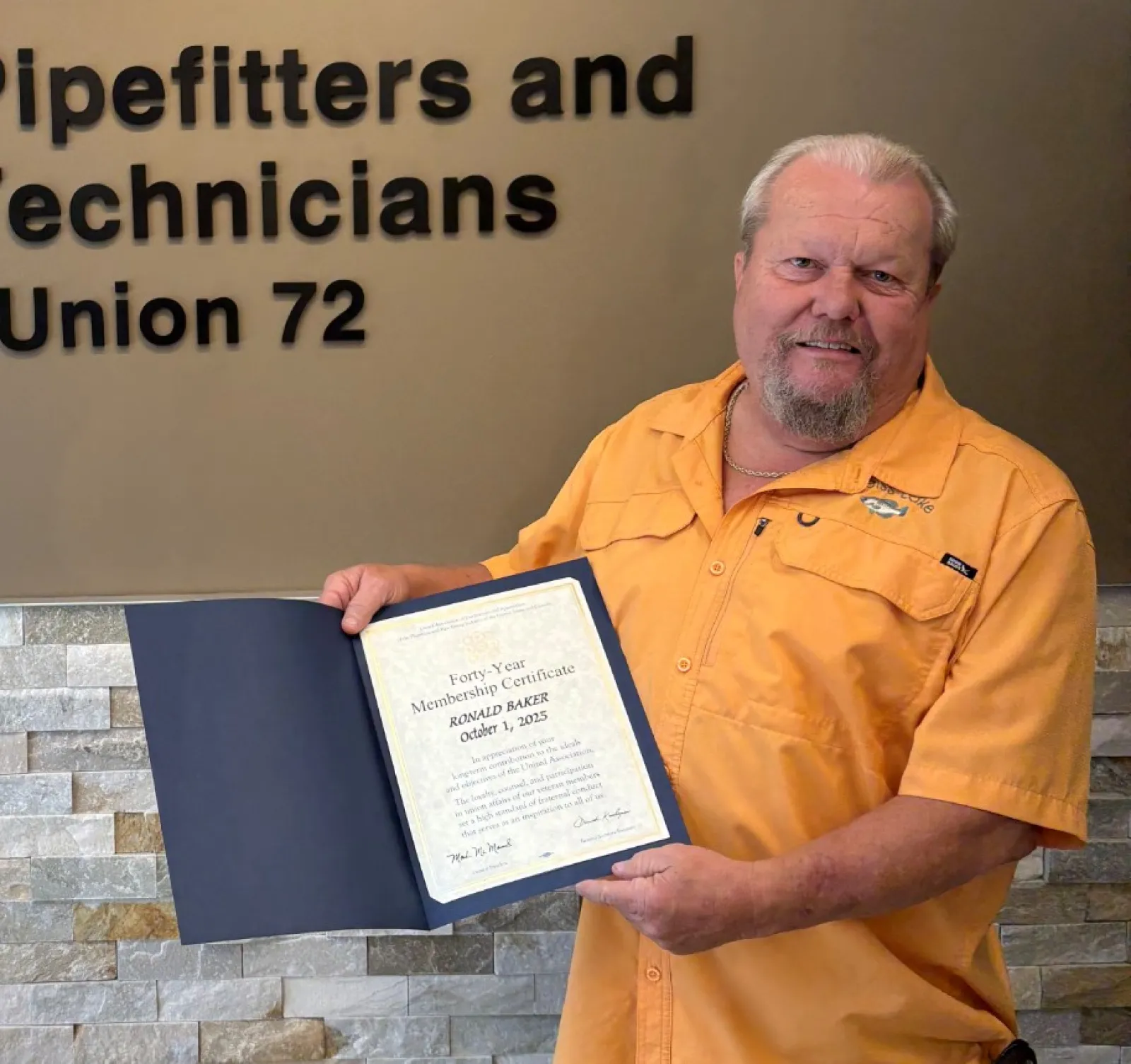 Man holding certificate standing next to Plumbers, Pipefitters and HVACR Technicians Local Union 72 sign indoors.