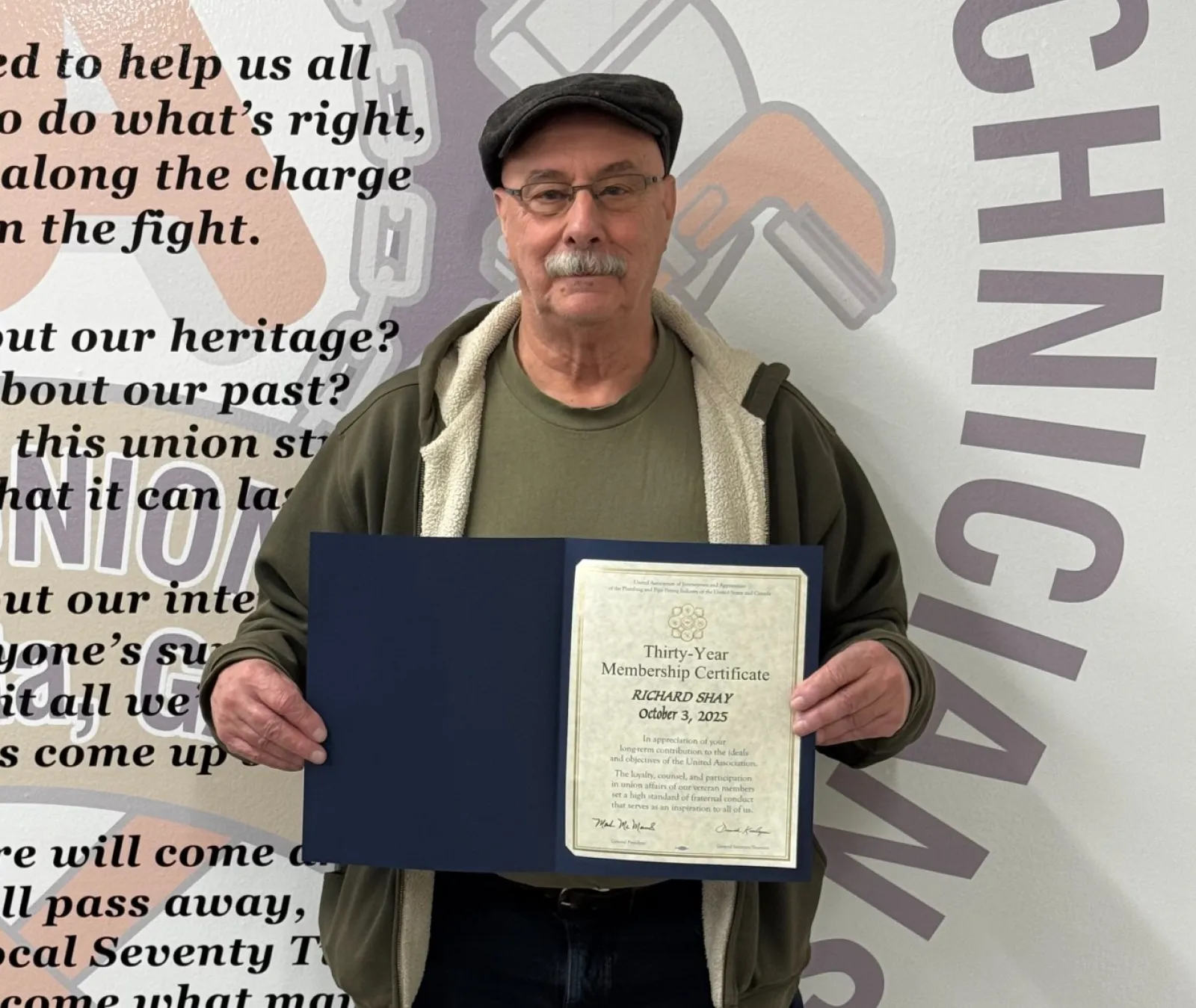 Man holding a thirty-year membership certificate standing in front of a wall with union text and graphics.