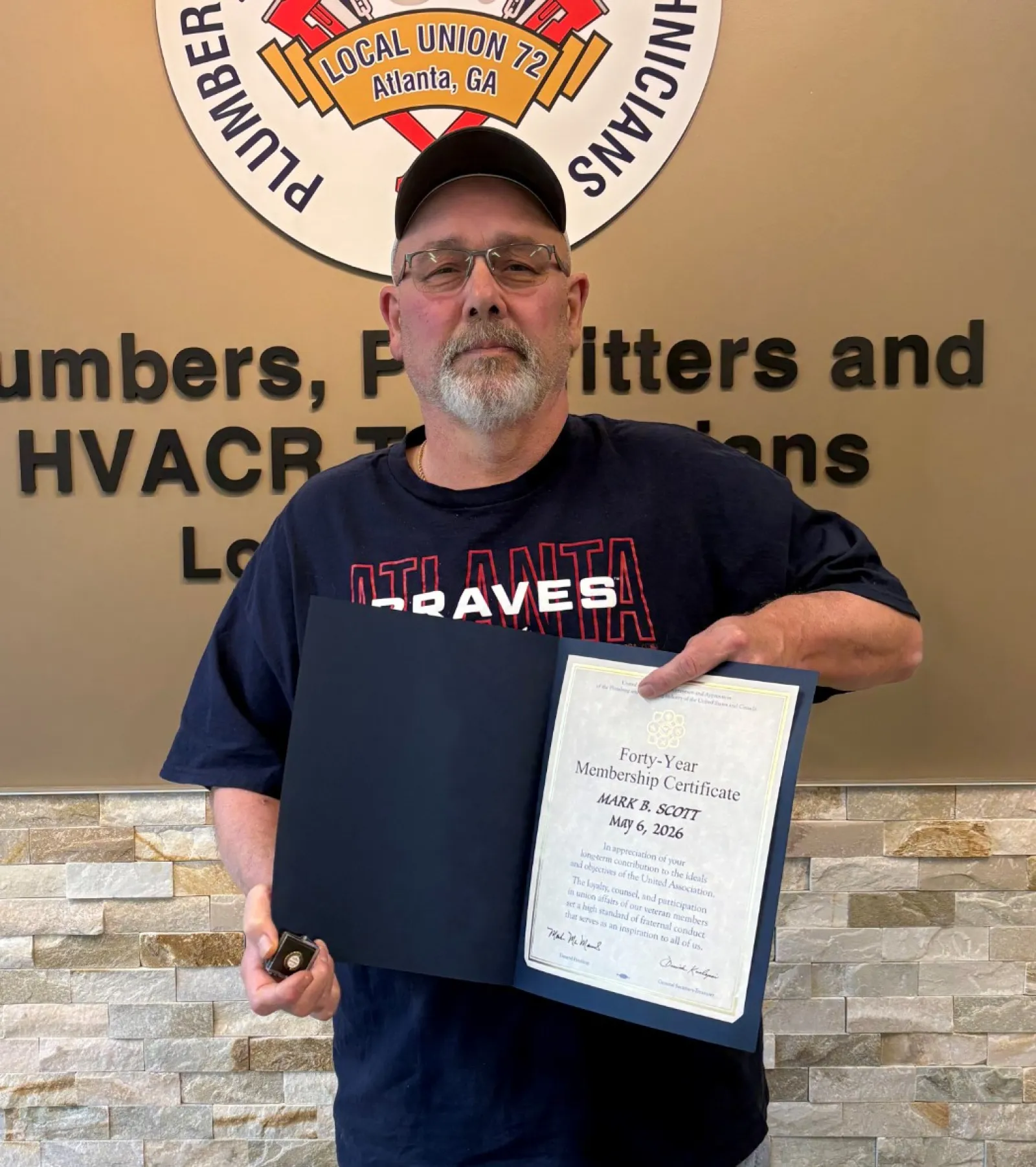 Man wearing a cap and glasses holding a certificate and key standing by a union service technicians logo and text.
