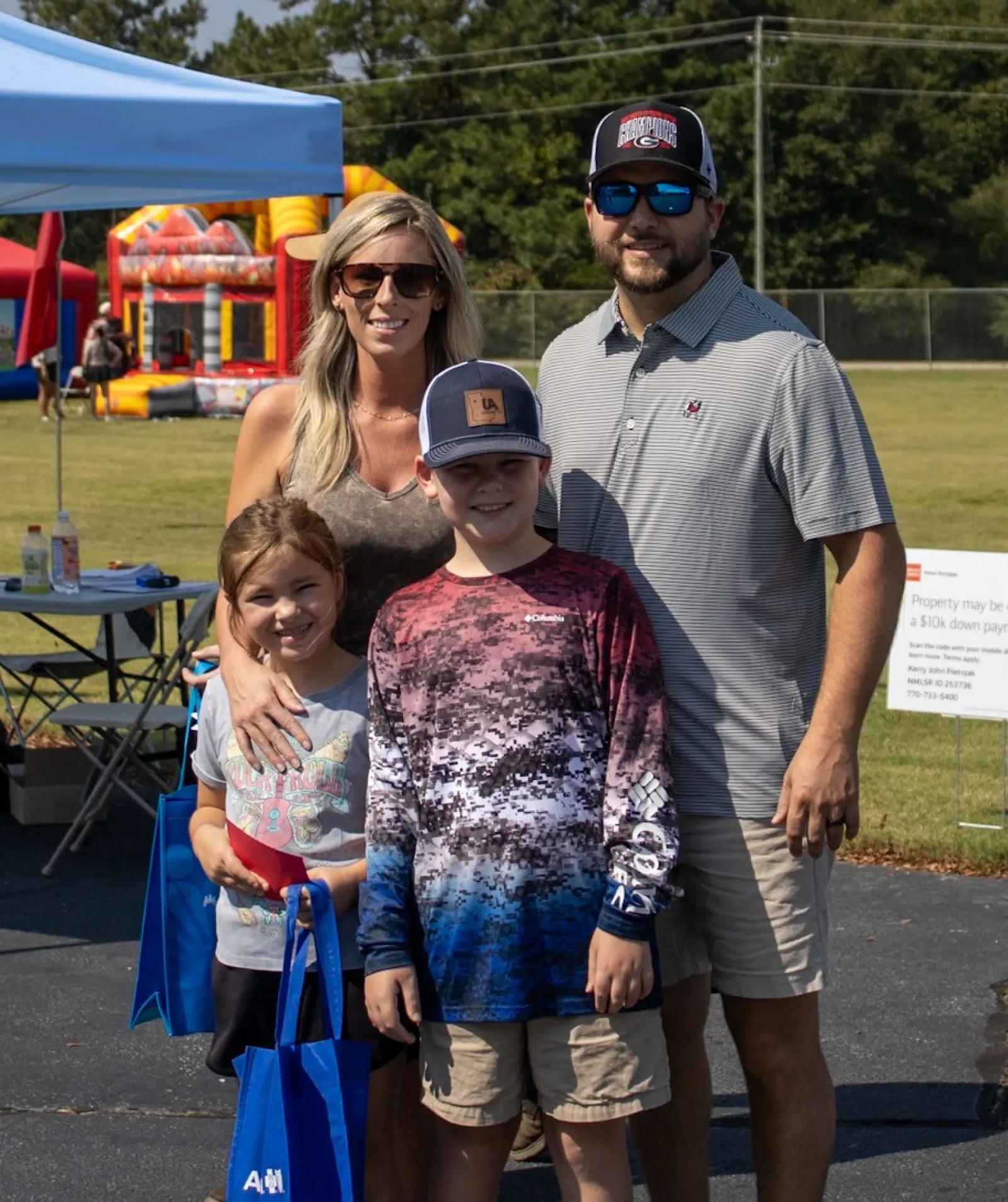 Family of four posing at outdoor festival with tents, inflatable bounce houses, and sunny weather