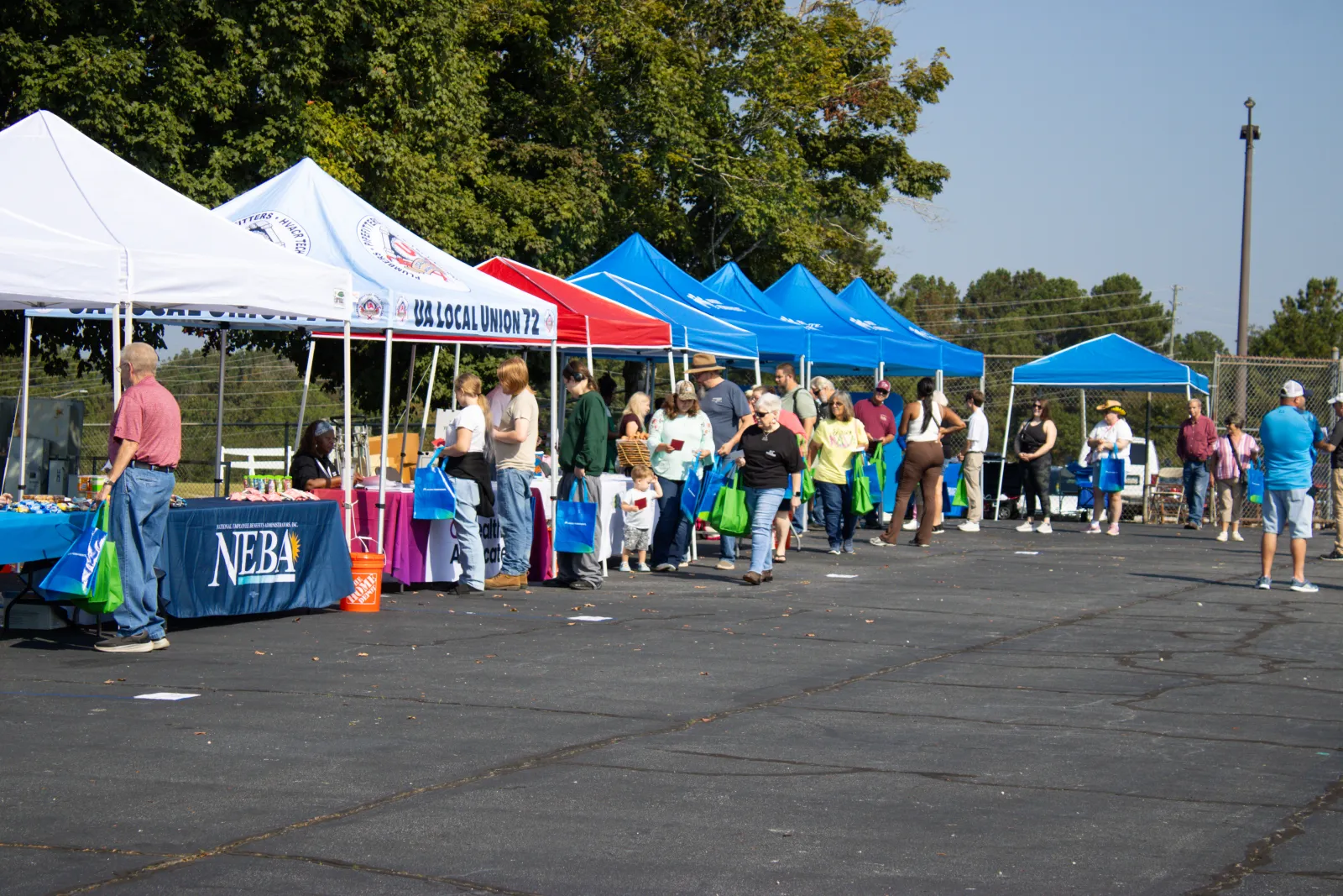 People gather at an outdoor event with tents and booths offering information and goods on a sunny day.
