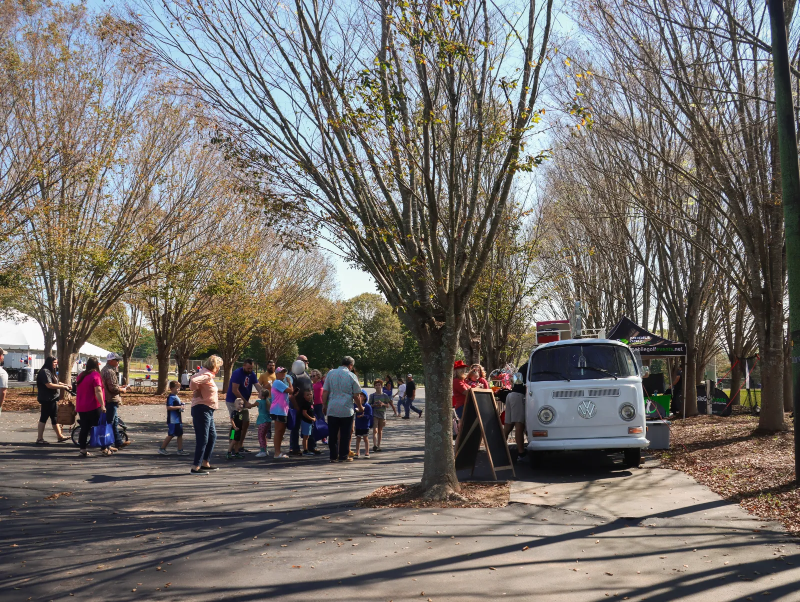 a group of people walking on a street with trees and a van