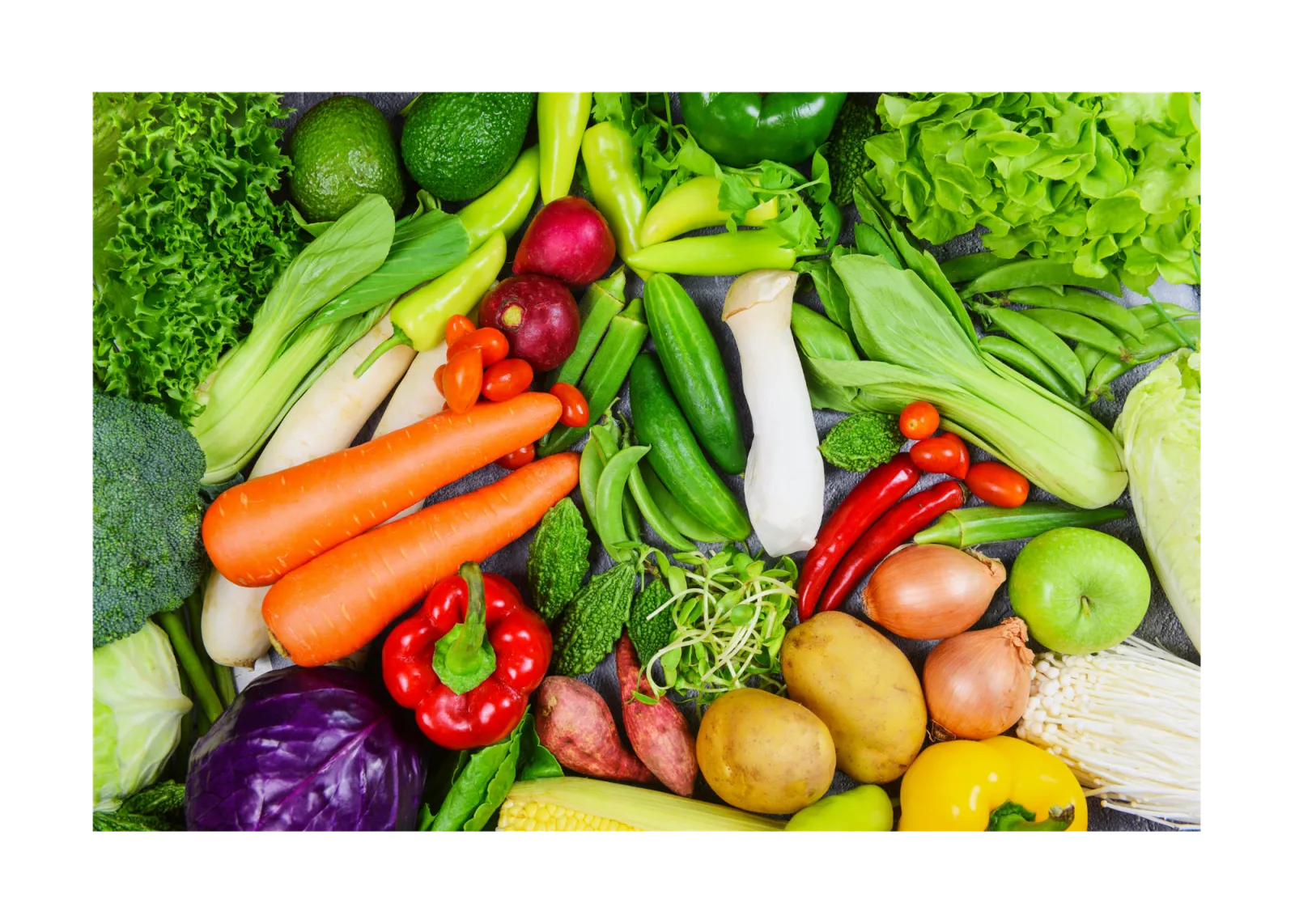 A group of vegetables are all bunched together on a table. Some of the foods include carrots, lettuce, peppers, cucumbers, potatoes, apples, celery and more.