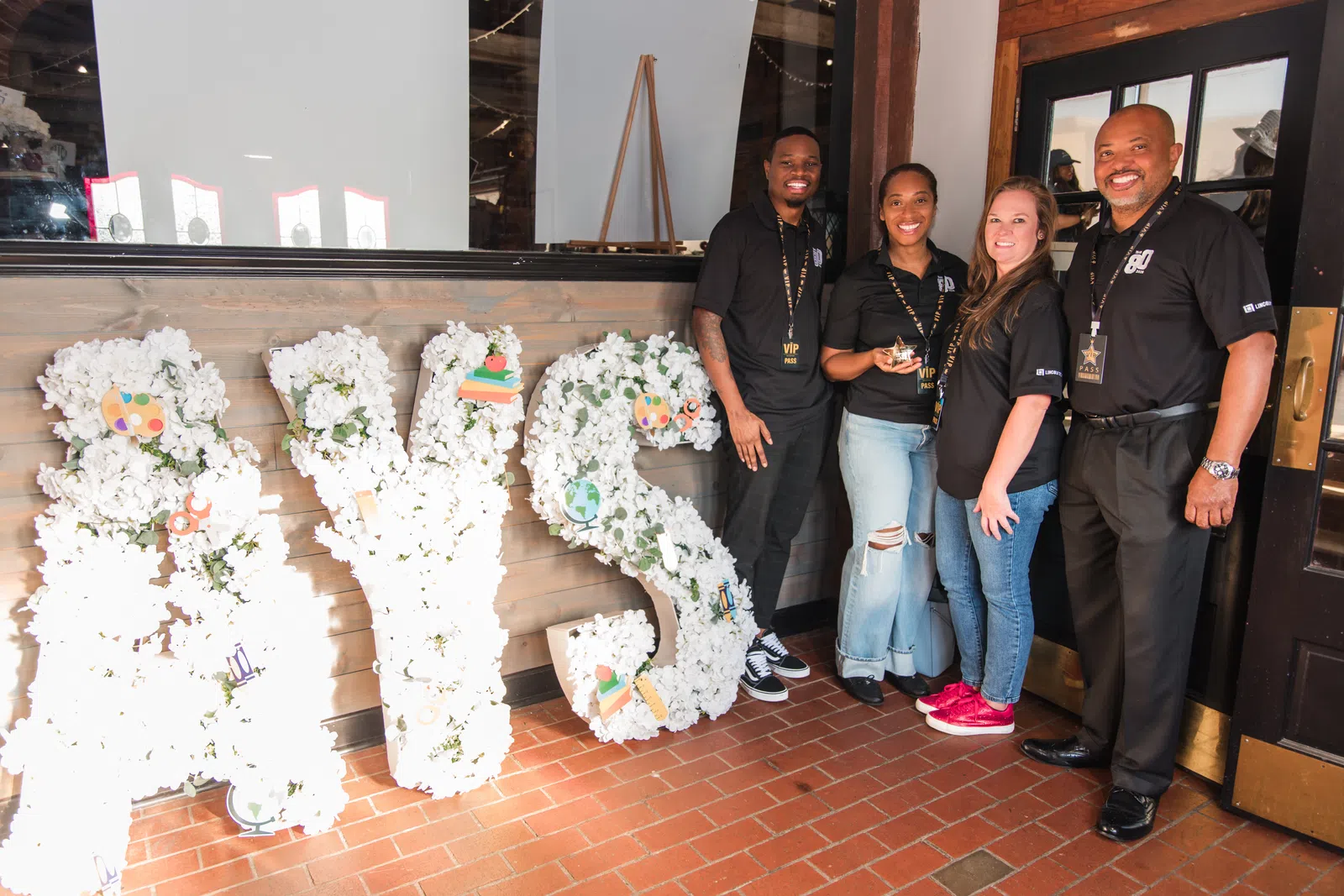 Four people standing beside large white floral letters spelling RYSE in a bright indoor space with wooden walls.