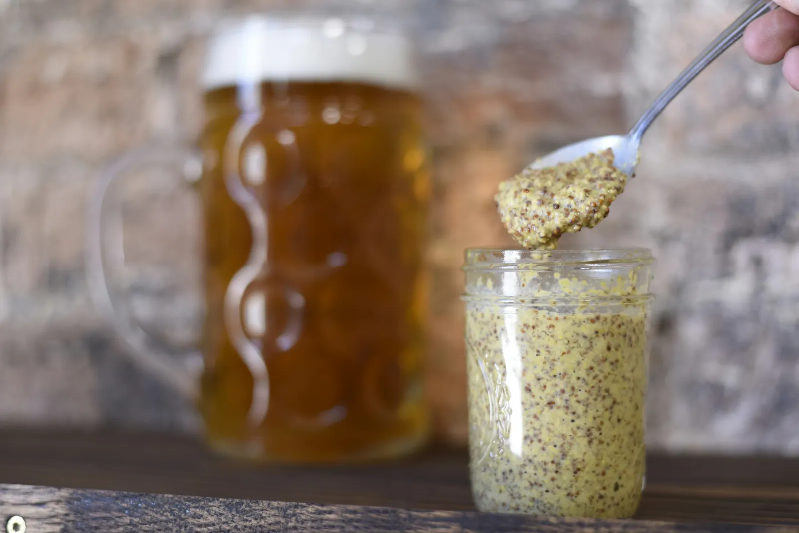 Close up of a glass jar of mustard with a mug of yellow beer in the background