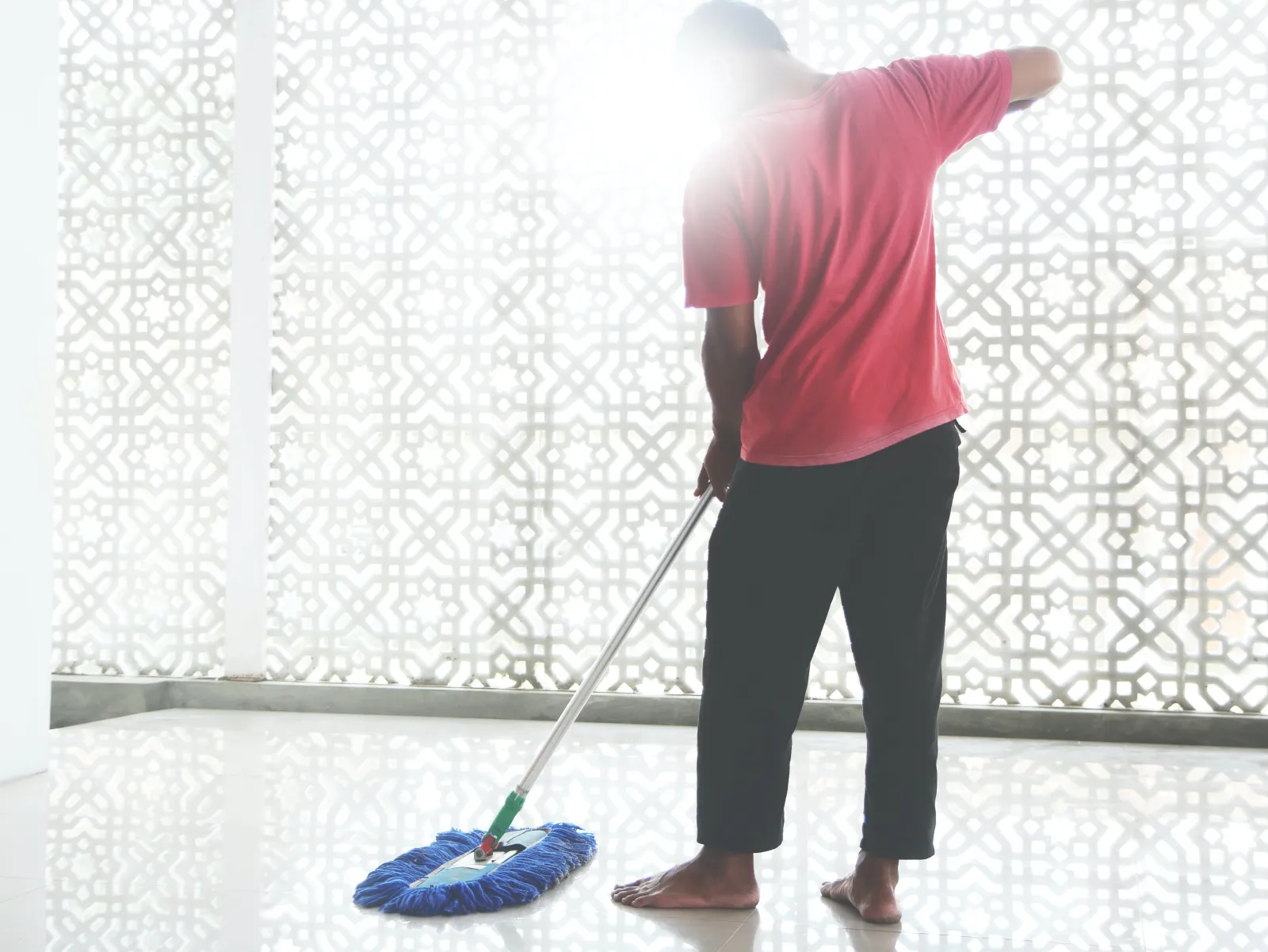 black man mopping floor barefoot with blue mop in a white room
