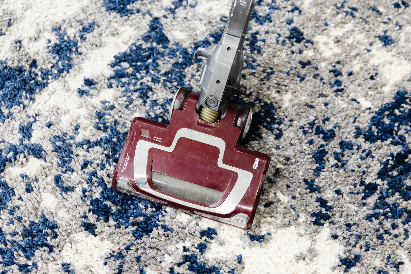 top down look at a red vacuum being used on a white, gray, and blue rug 