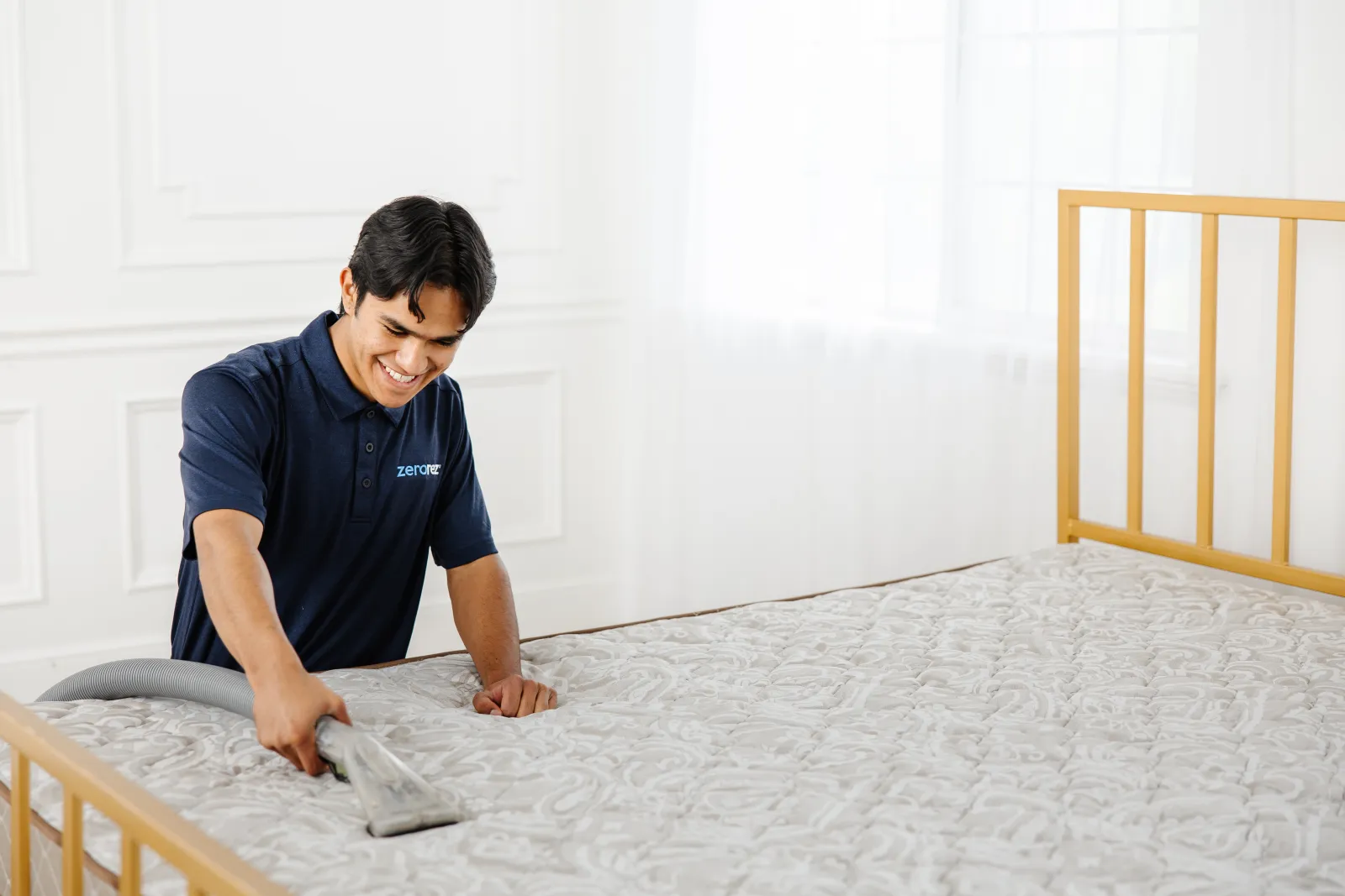 a male Zerorez technician using an upholstery tool to professionally clean a mattress in a bedroom