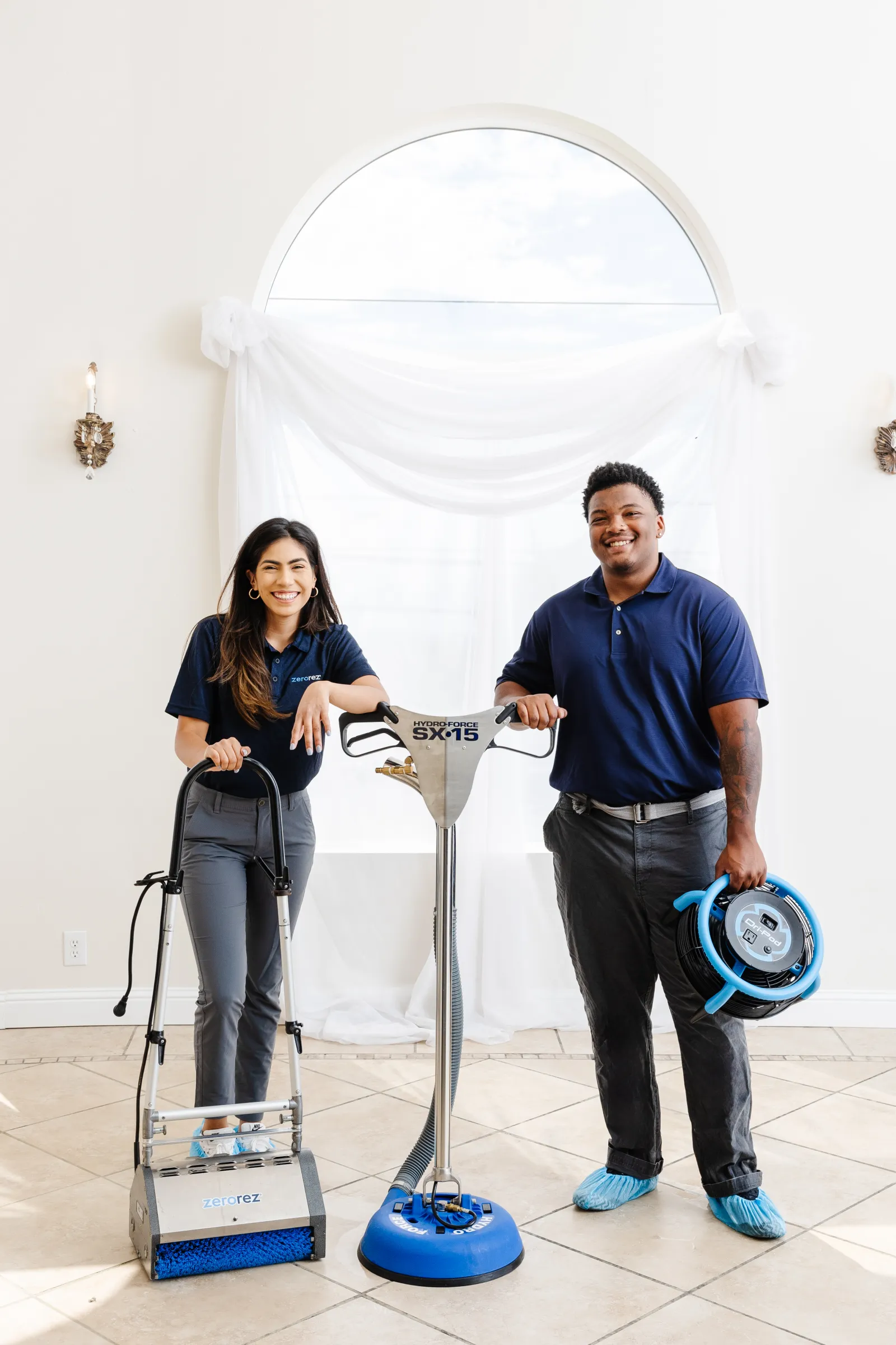 smiling female and male Zerorez cleaning technicians standing on porcelain tile floor with various tile and grout cleaning tools and equipment