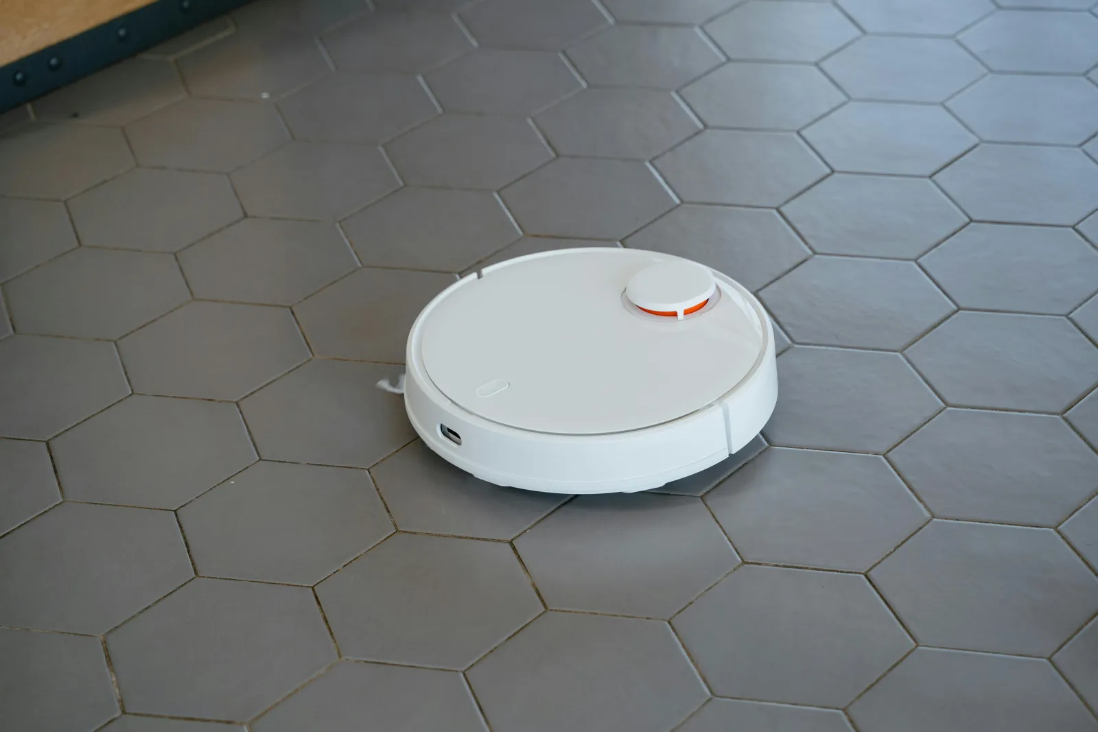 small white robot vacuum cleaning gray hexagon tile floor