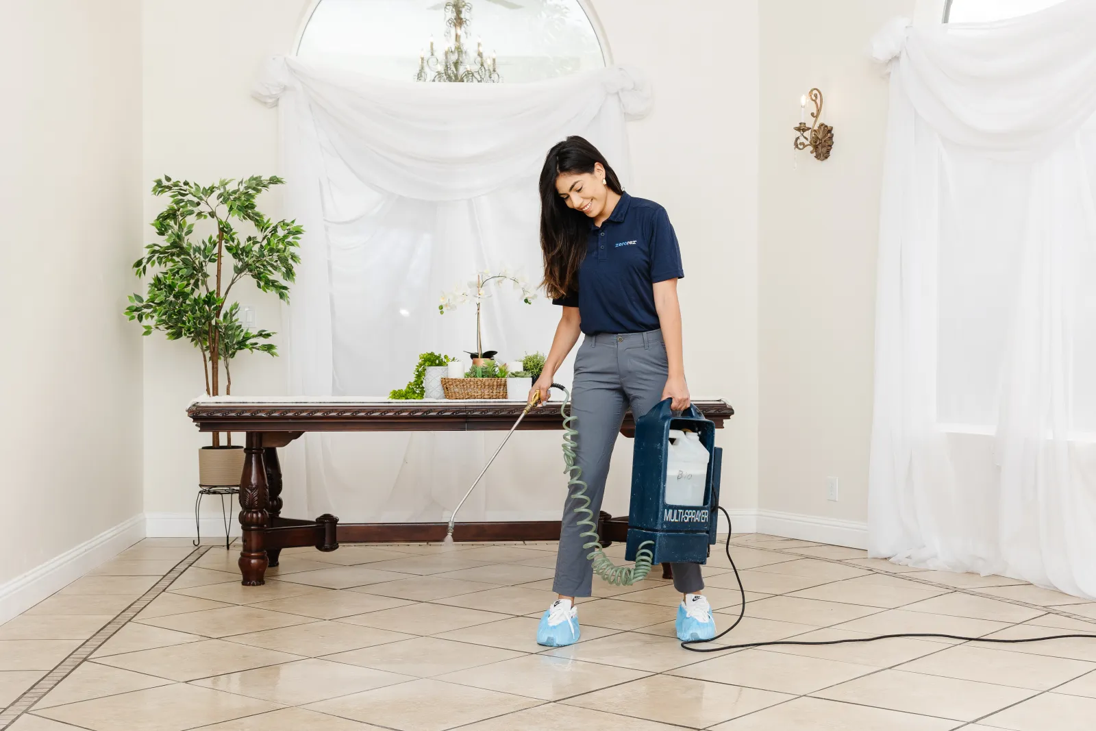 Female Zerorez® technician spraying a pretreatment to a porcelain tile floor in a dining room area before she cleans it with the best tile floor cleaning system which is Zerorez professional tile cleaning services