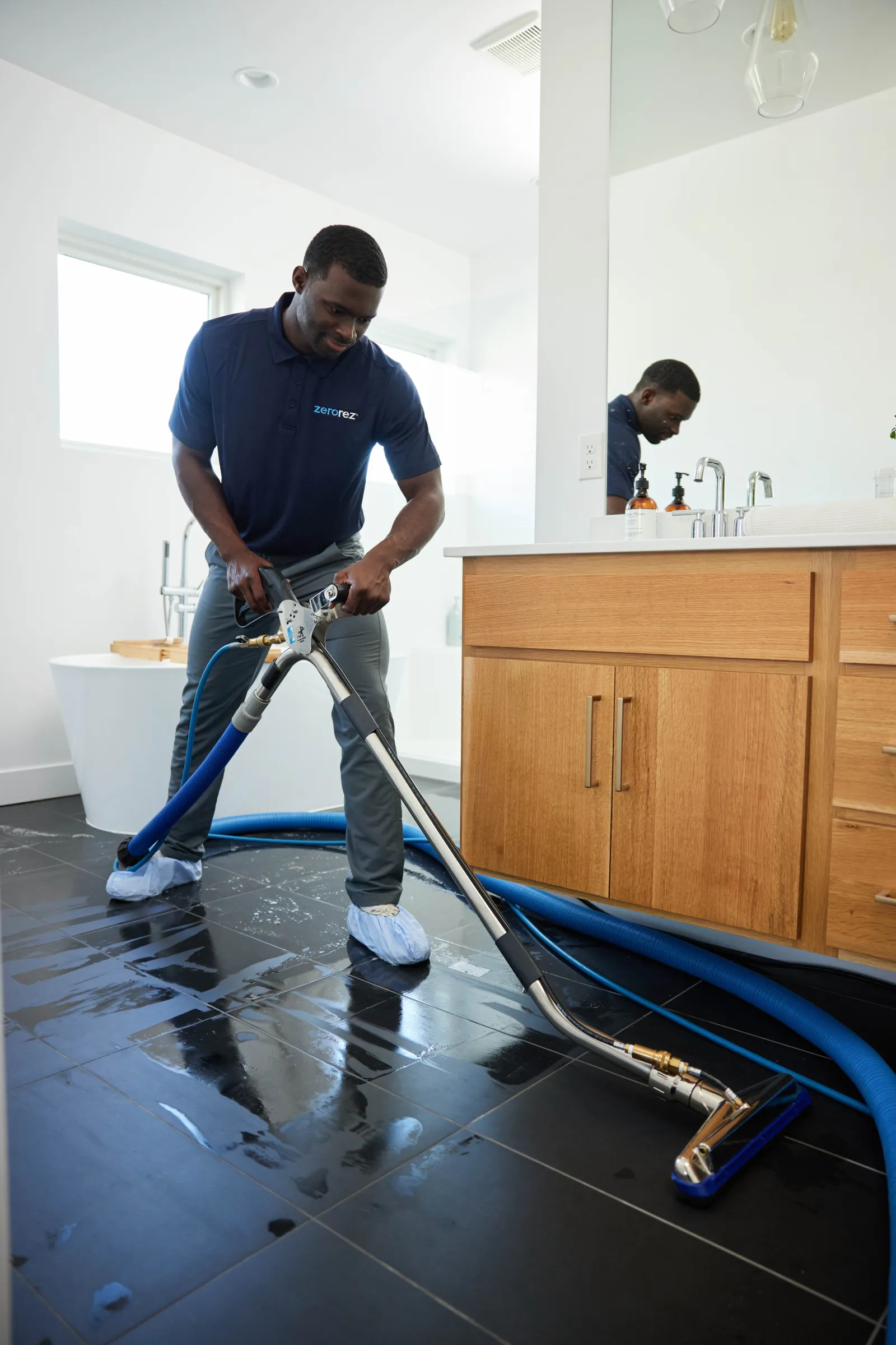 a male Zerorez® technician cleaning a black porcelain tile floor in a residential bathroom with the Zr™ Wand