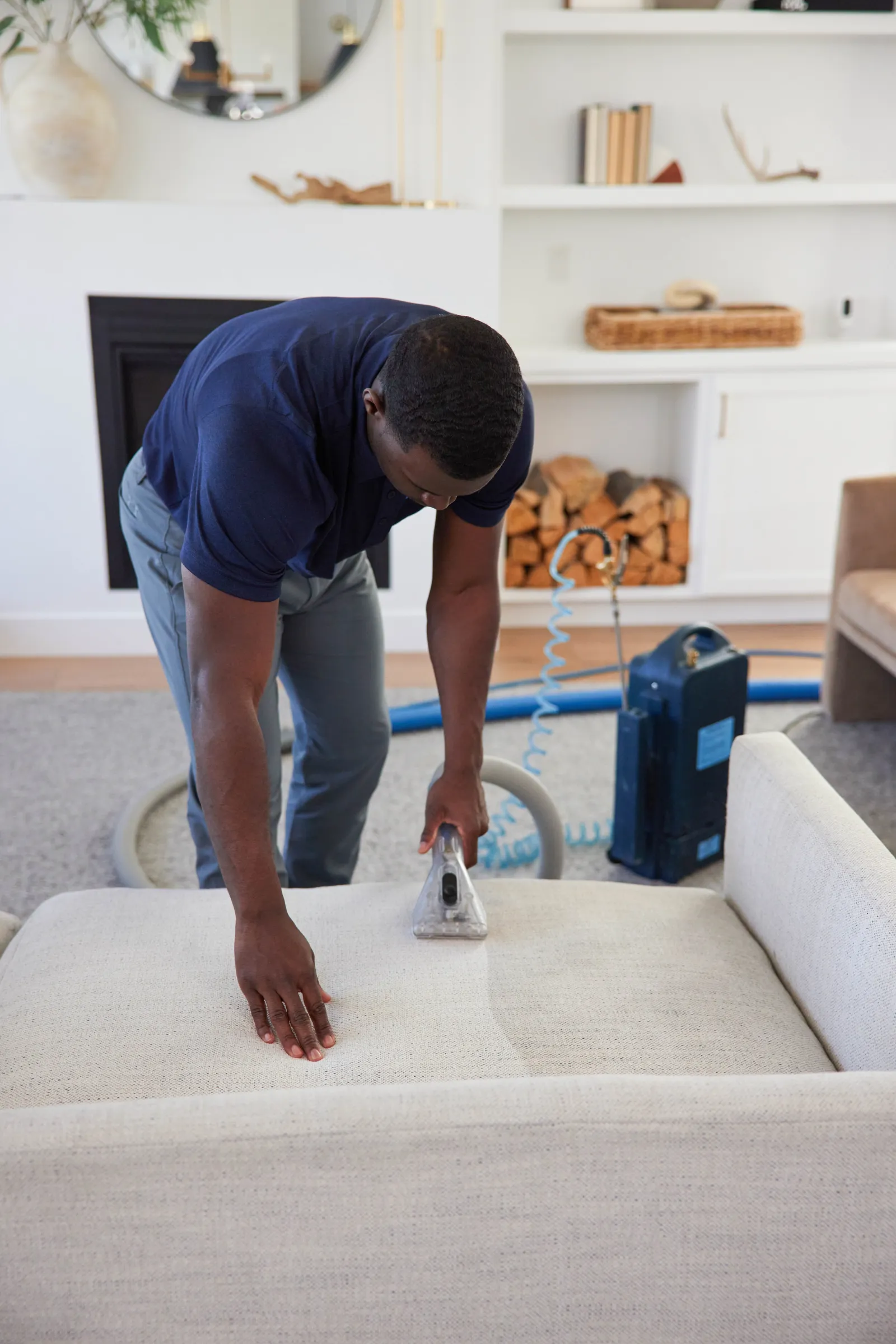 a black Zerorez® technician expertly cleaning a white couch in a living room using professional upholstery tools, pre-spray, and extraction tool