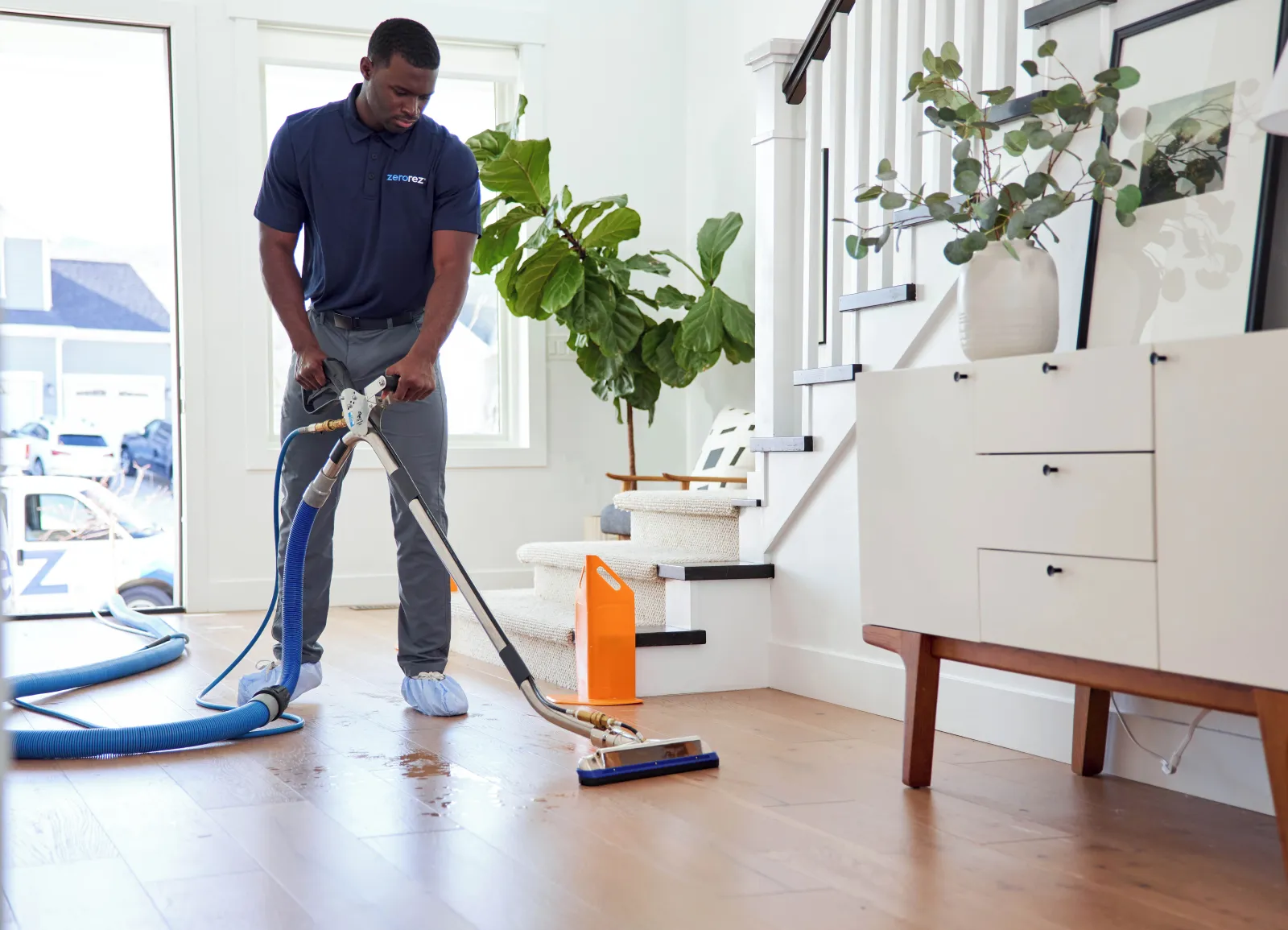 black male Zerorez technician using specialized Zr­™ Wand to clean a hardwood floor