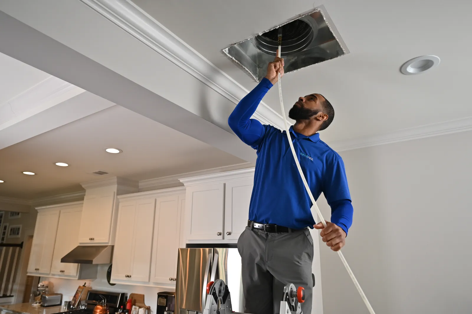 a male Zerorez technician cleaning a ceiling HVAC air duct register in a residential home