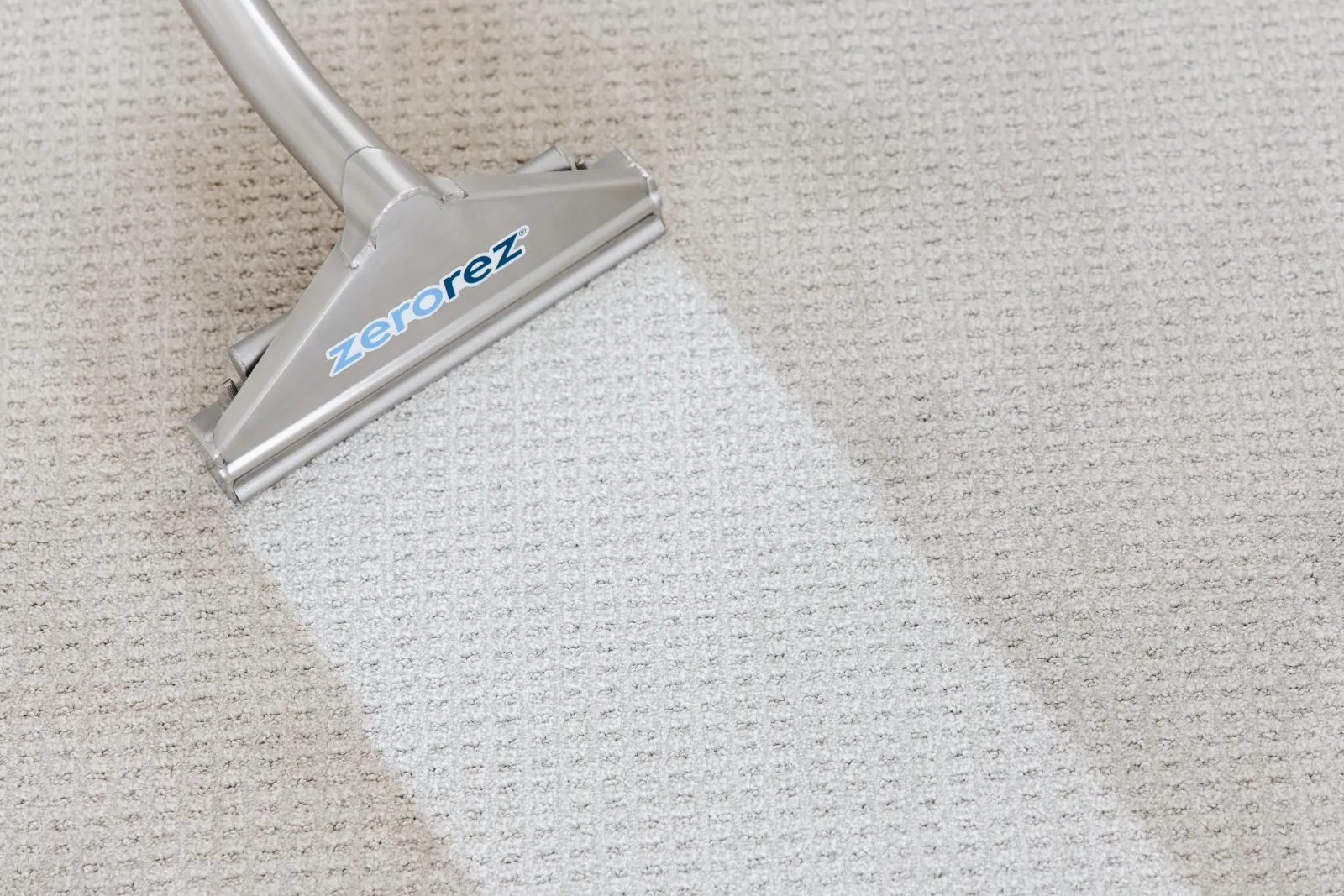 Close up of a Zerorez Zr Wand being used to clean a gray carpet of dirt, showing a clean white path