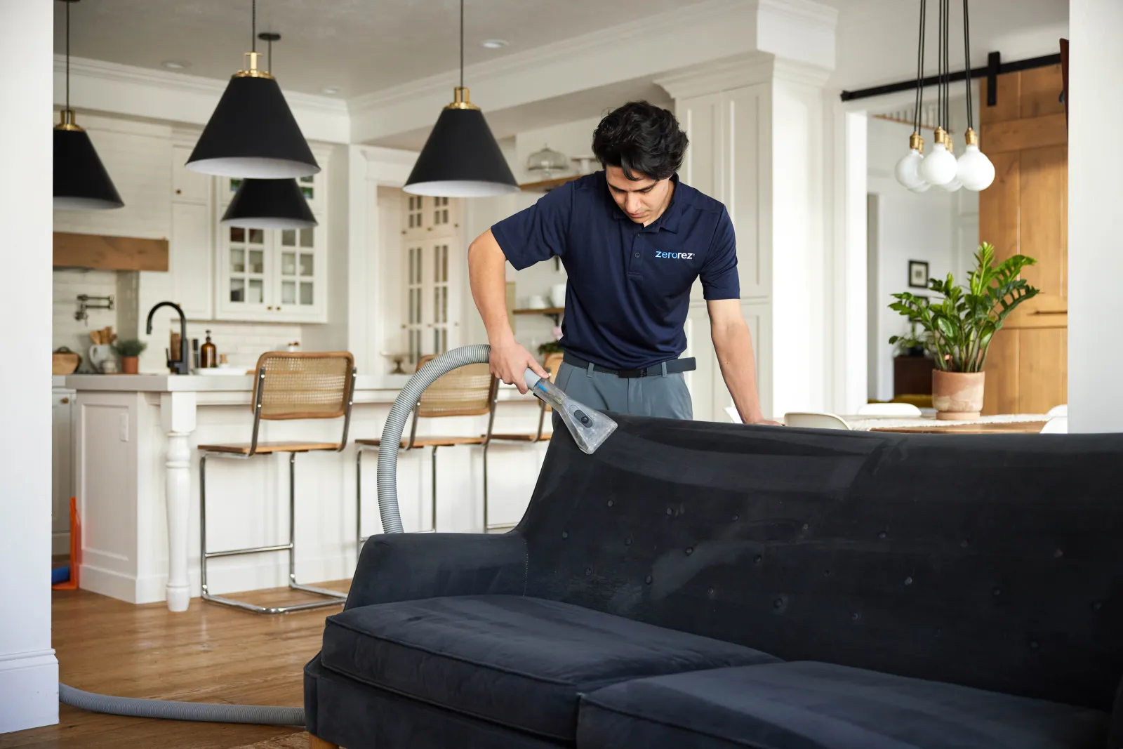 male Zerorez technician standing behind a navy blue couch using a handheld upholstery cleaning tool to spot clean microfiber couch and ensure it doesn't get water spots