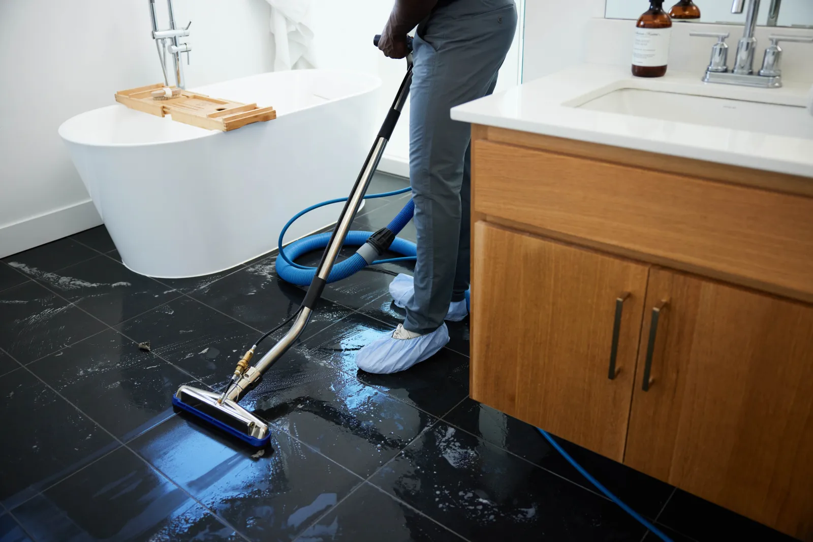 Zerorez technician cleaning a black porcelain tile floor with a silver extraction wand in a bathroom