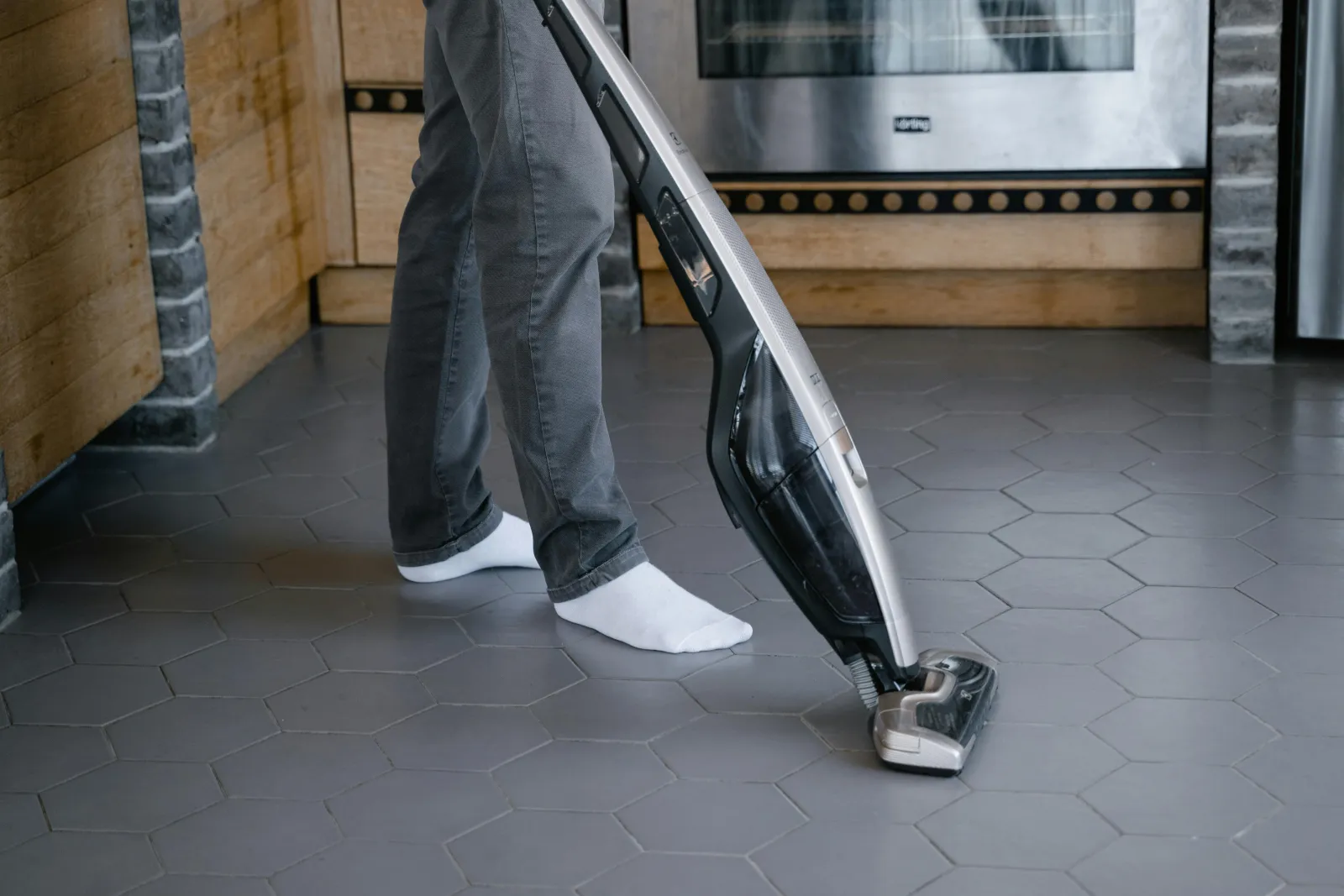 socked feet standing on a gray hexagon tile floor using a vacuum on tile