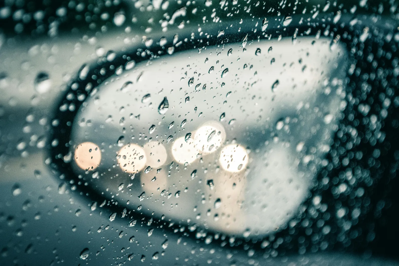 close up of water droplets and condensation inside a car looking at side view mirror of a wet car in rain