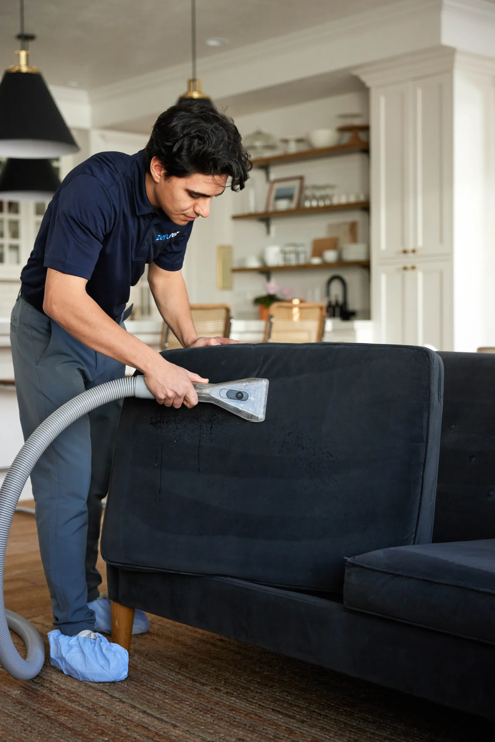 male Zerorez cleaning technician using a handheld upholstery cleaning tool to professionally clean a microfiber couch cushion