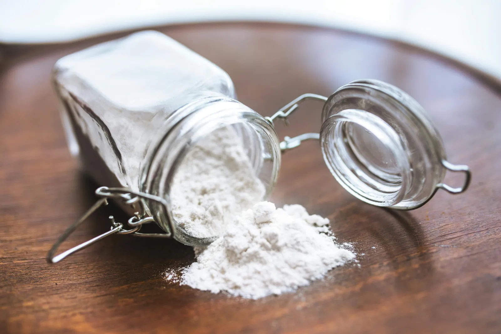 baking soda spilling out of a small glass container on a wood surface