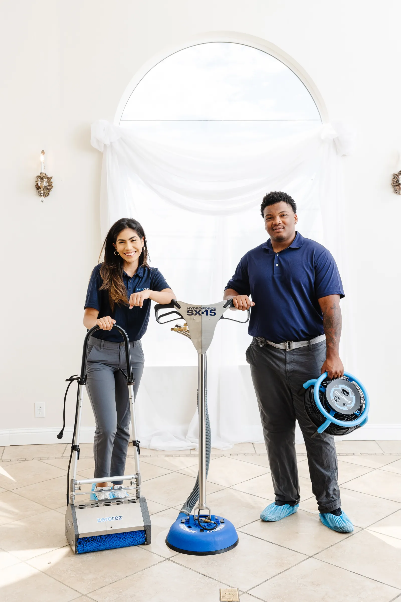 a female and male Zerorez® technician standing with various porcelain tile floor cleaning tools and equipment, smiling at the camera and ready to help you clean