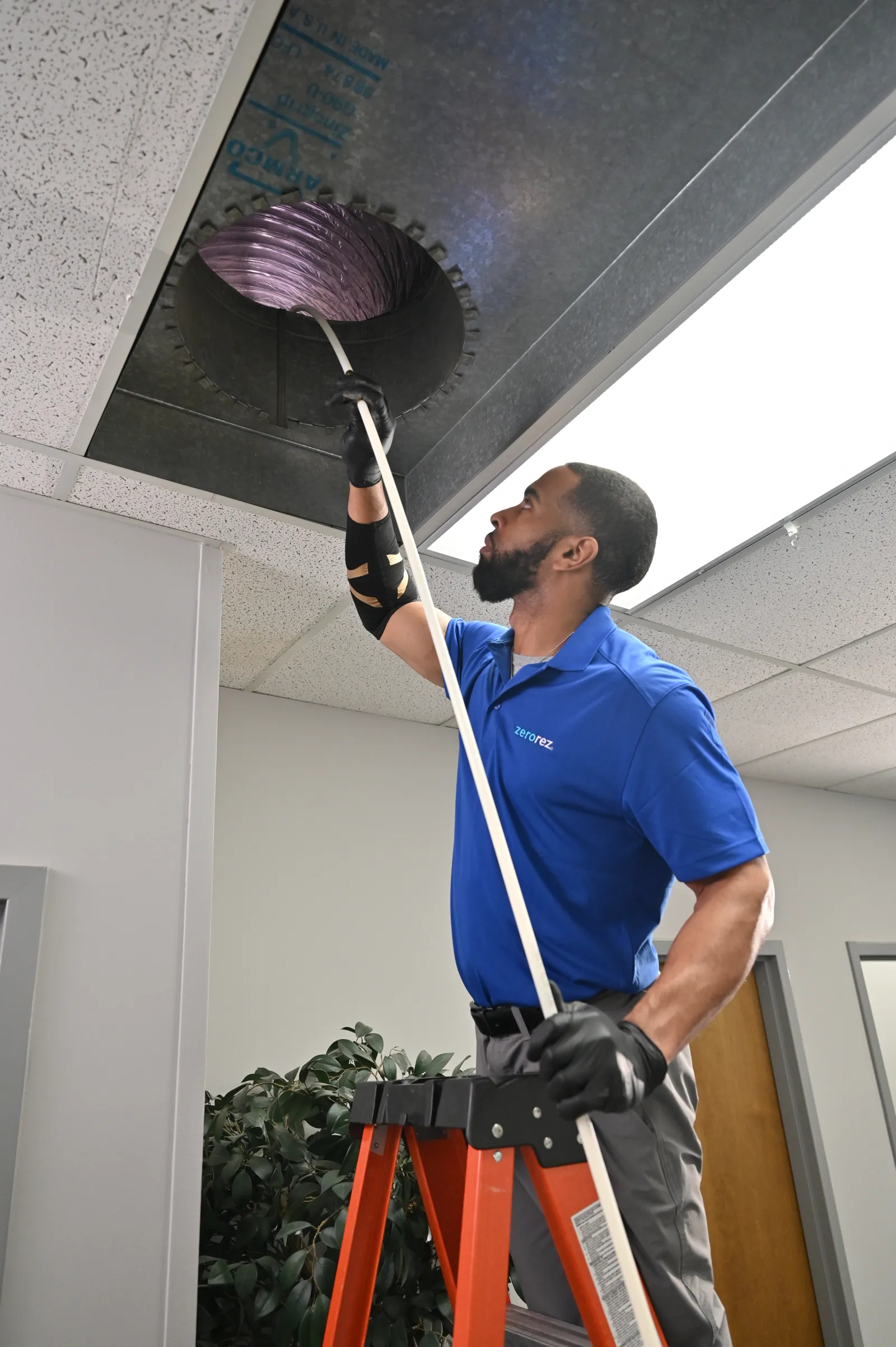 male Zerorez technician standing on a ladder to clean air ducts in the ceiling