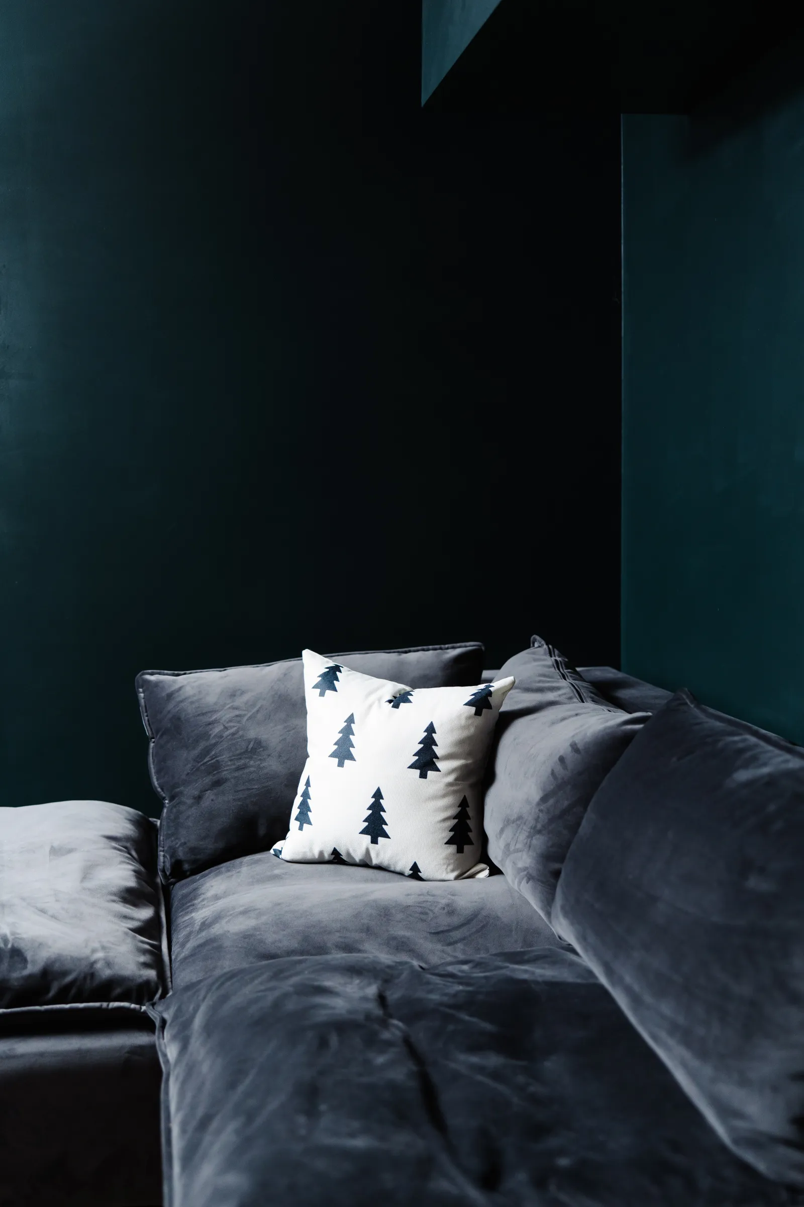 Picture of a dark gray suede couch in a dark black-painted room with a Christmas tree black and white pillow on it