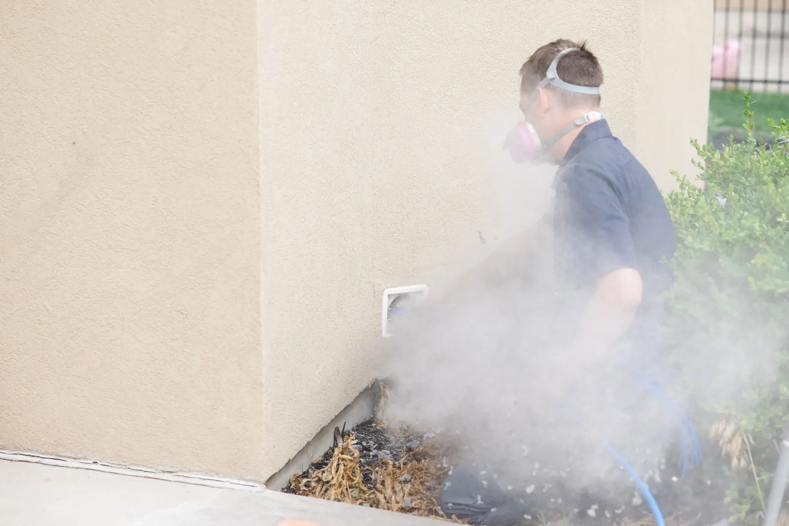 Male Zerorez technician kicking out a lot of lint and debris from an external dryer vent hose, while wearing a face mask