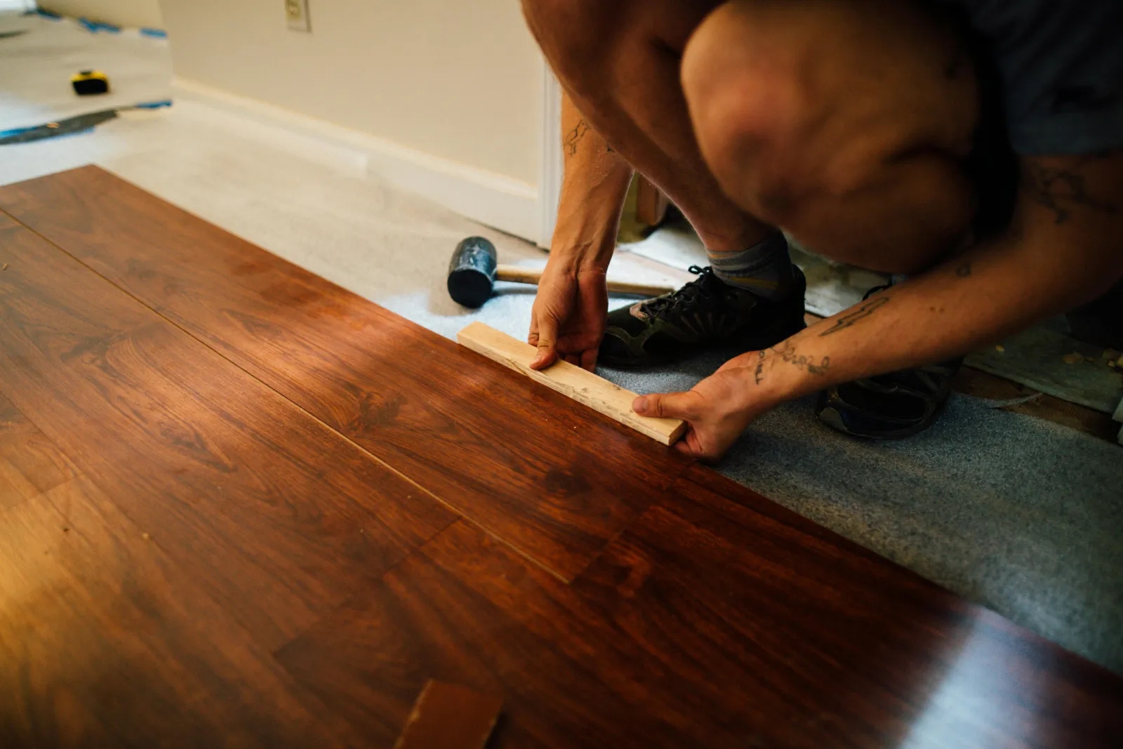 Man squatting down to install a laminate faux wood floor on top of an underlayment