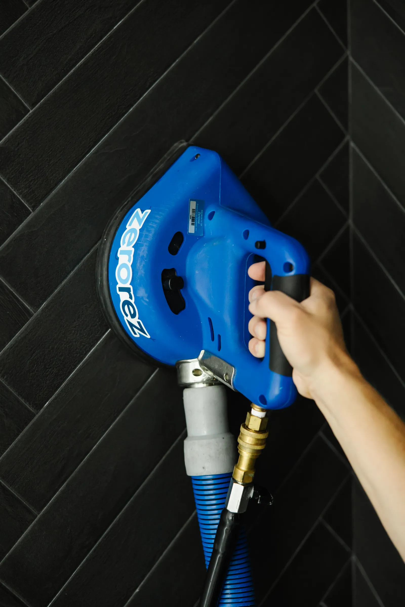 close up of Zerorez® handheld tile and grout cleaning tool being used on black tiles with white grout lines