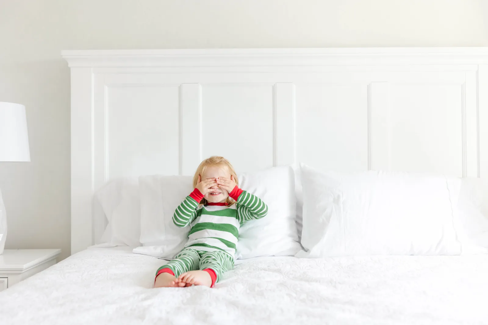 toddler in pajamas playing on white bed and mattress