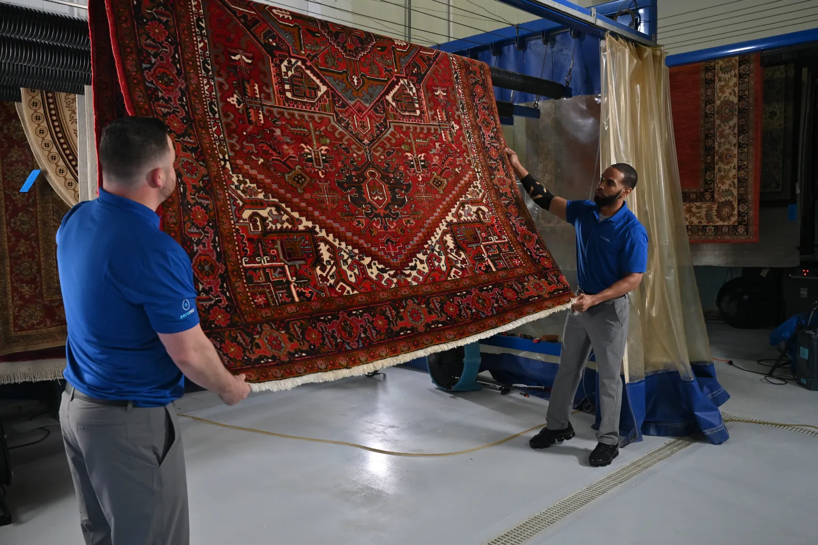 Two male Zerorez technician handling a pretty red oriental wool carpet in a carpet cleaning rug spa