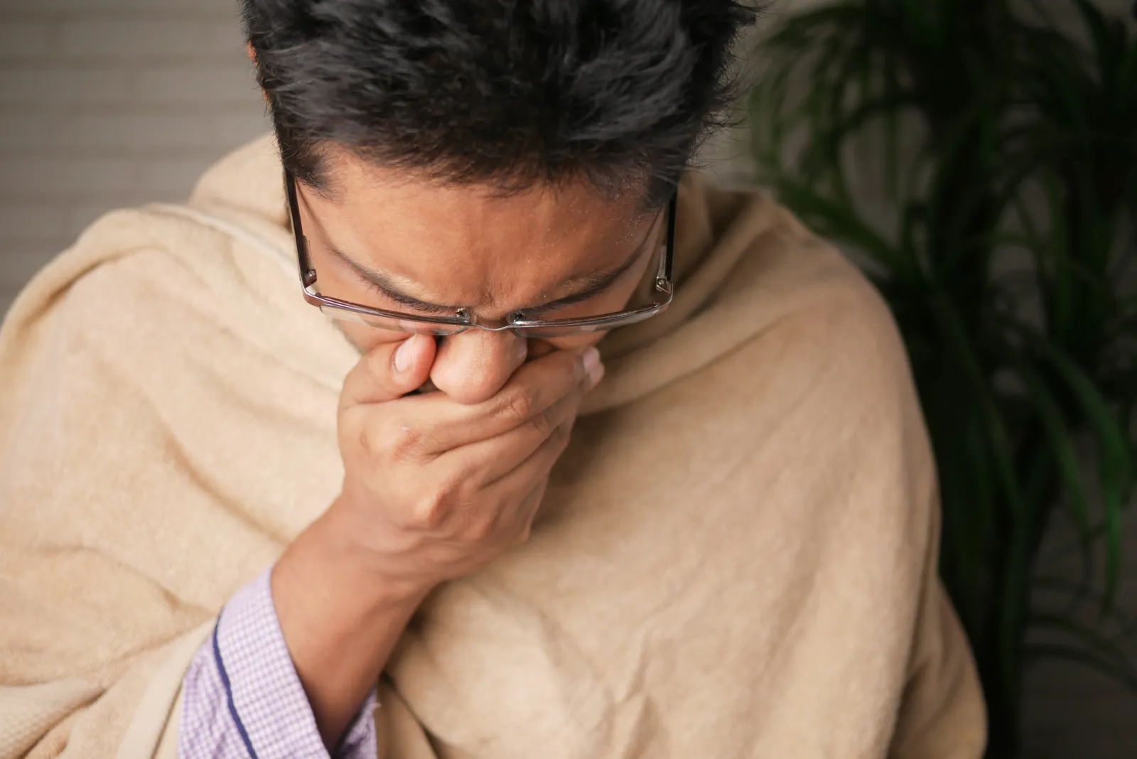 A man wearing glasses, covering his nose with his hand and sneezing into his hand as he suffers from dirty air ducts causing allergies