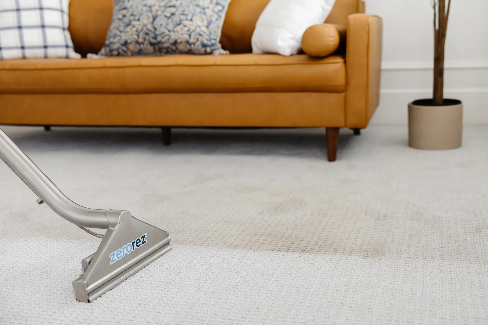 Close up of a Zerorez Zr Wand cleaning a textured gray carpet with a tan leather couch in the background