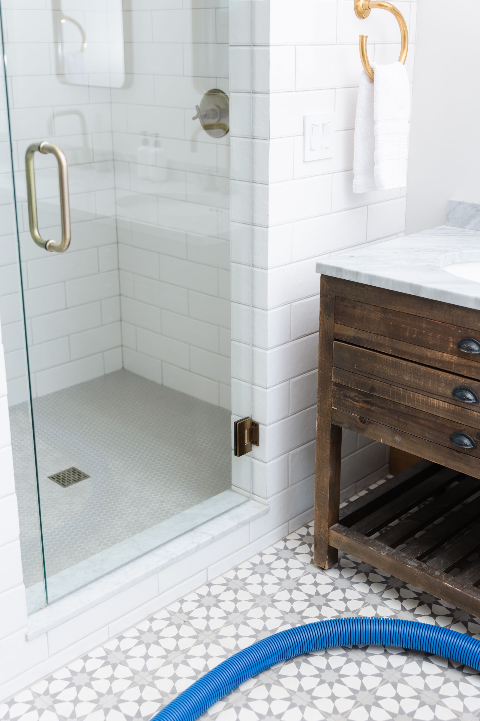 white tiled bathroom with glass door shower and a blue Zerorez® hose on the floor 