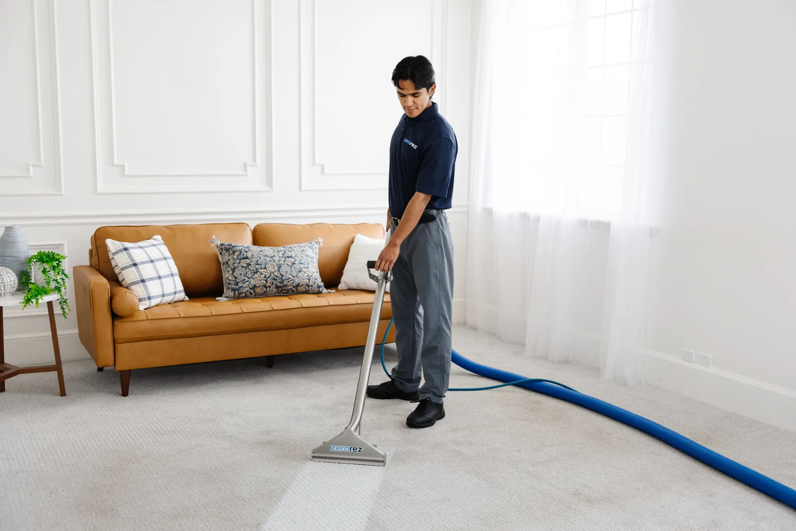 Professional Zerorez male technician cleaning a gray carpet in a living room, revealing a clean stripe in the carpet where the Zr Wand and Zr Water cleaned with an alkaline higher pH